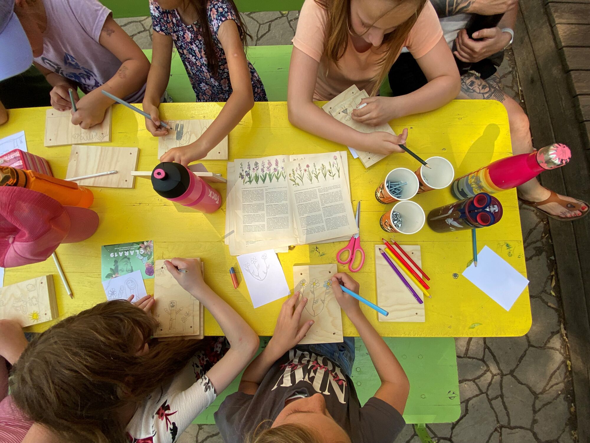 © SEB Leipzig Viele Kinder sitzen an einem Tisch und gestalten Blumenpressen mit Stiften