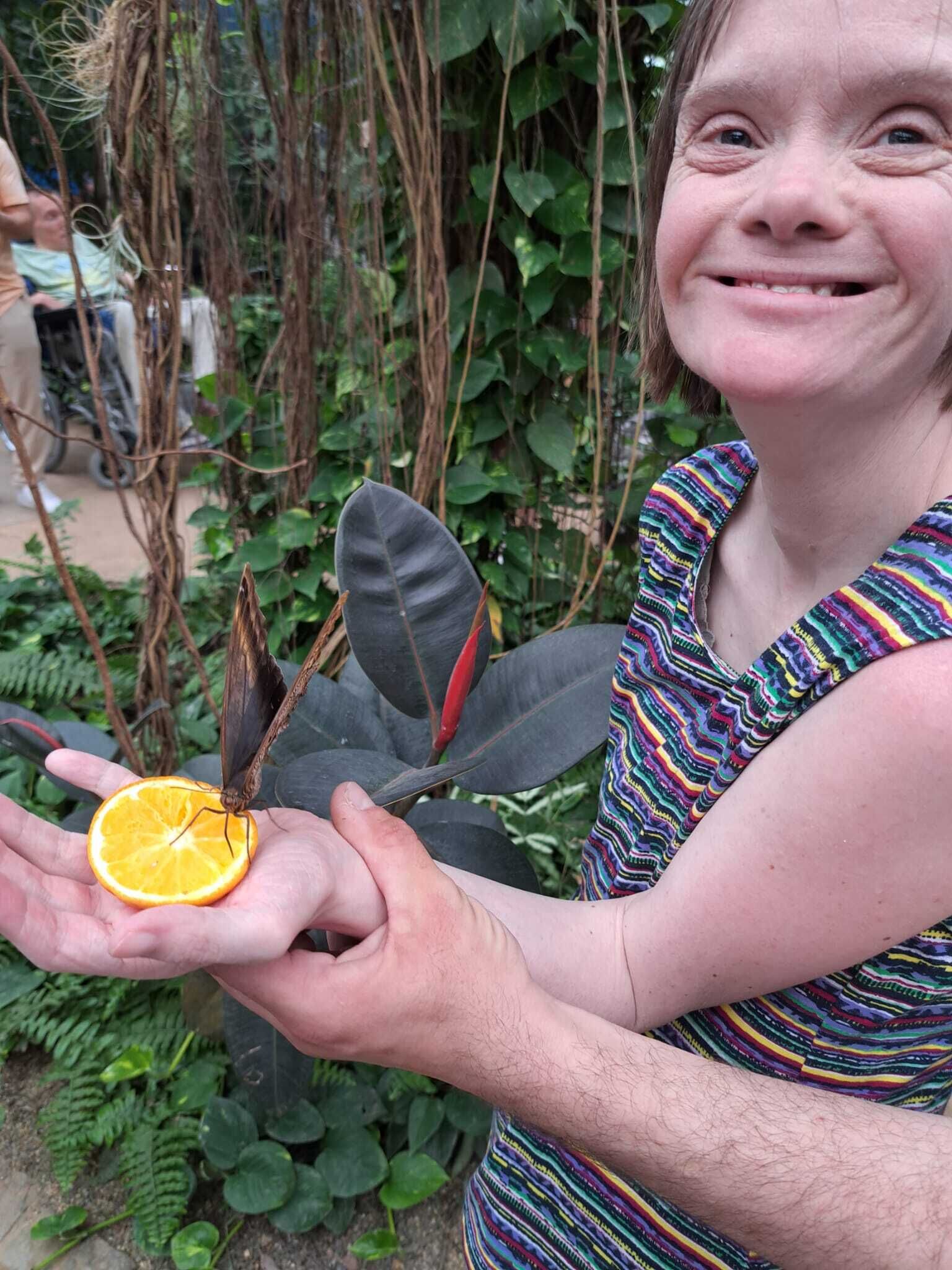 © SEB Leipzig Eine Frau hält eine Orangenscheibe in der Handfläche. Darauf sitzt ein großer Schmetterling.