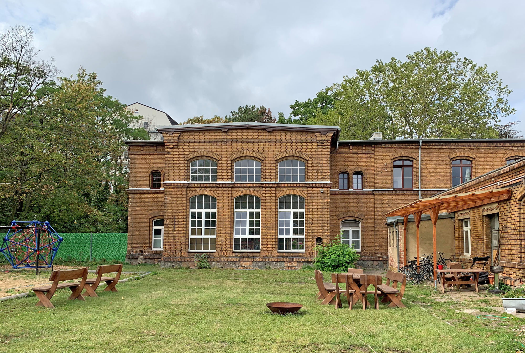 Ein Backsteingebäude in einem Garten mit Klettergerüst, Feuerschale und Sitzgelegenheiten.