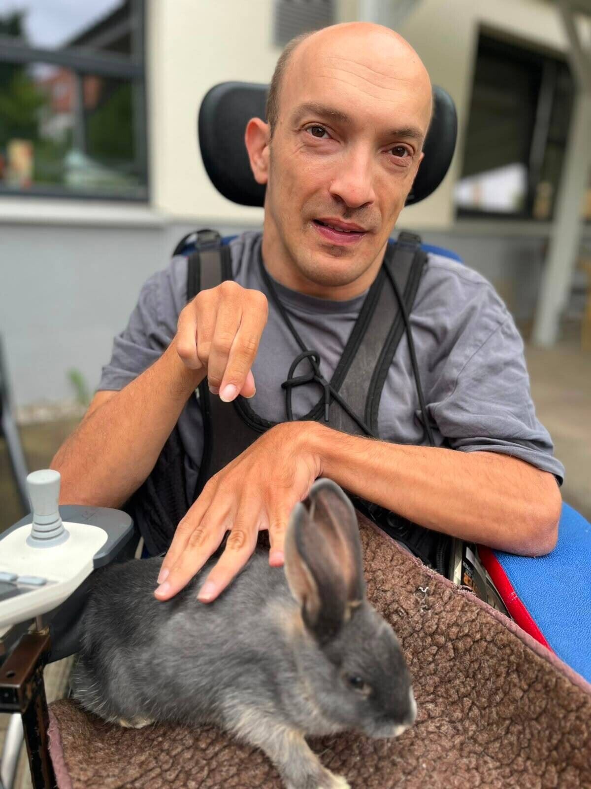 Ein Mann im Rollstuhl streichelt ein H&auml;schen