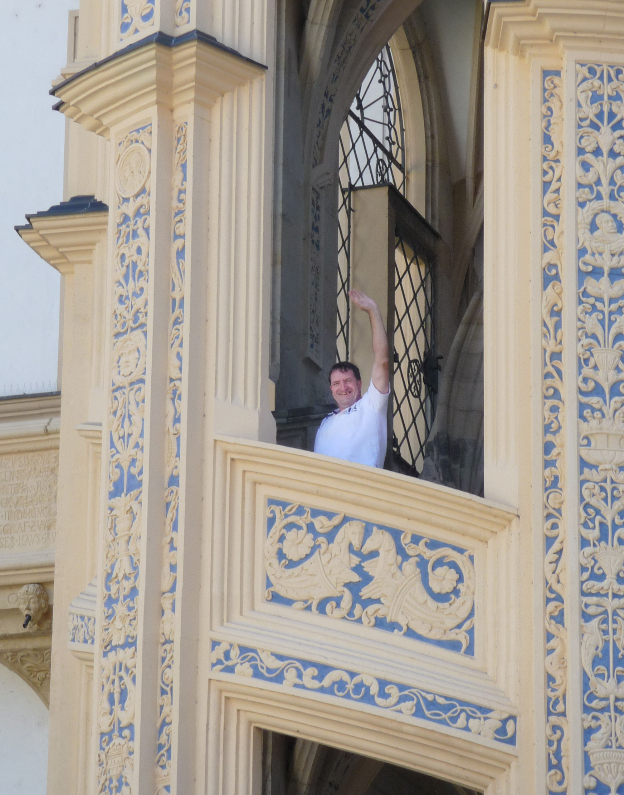 Ein Mann winkt von einem gelben Balkon mit blauen künstlerischen Elementen.