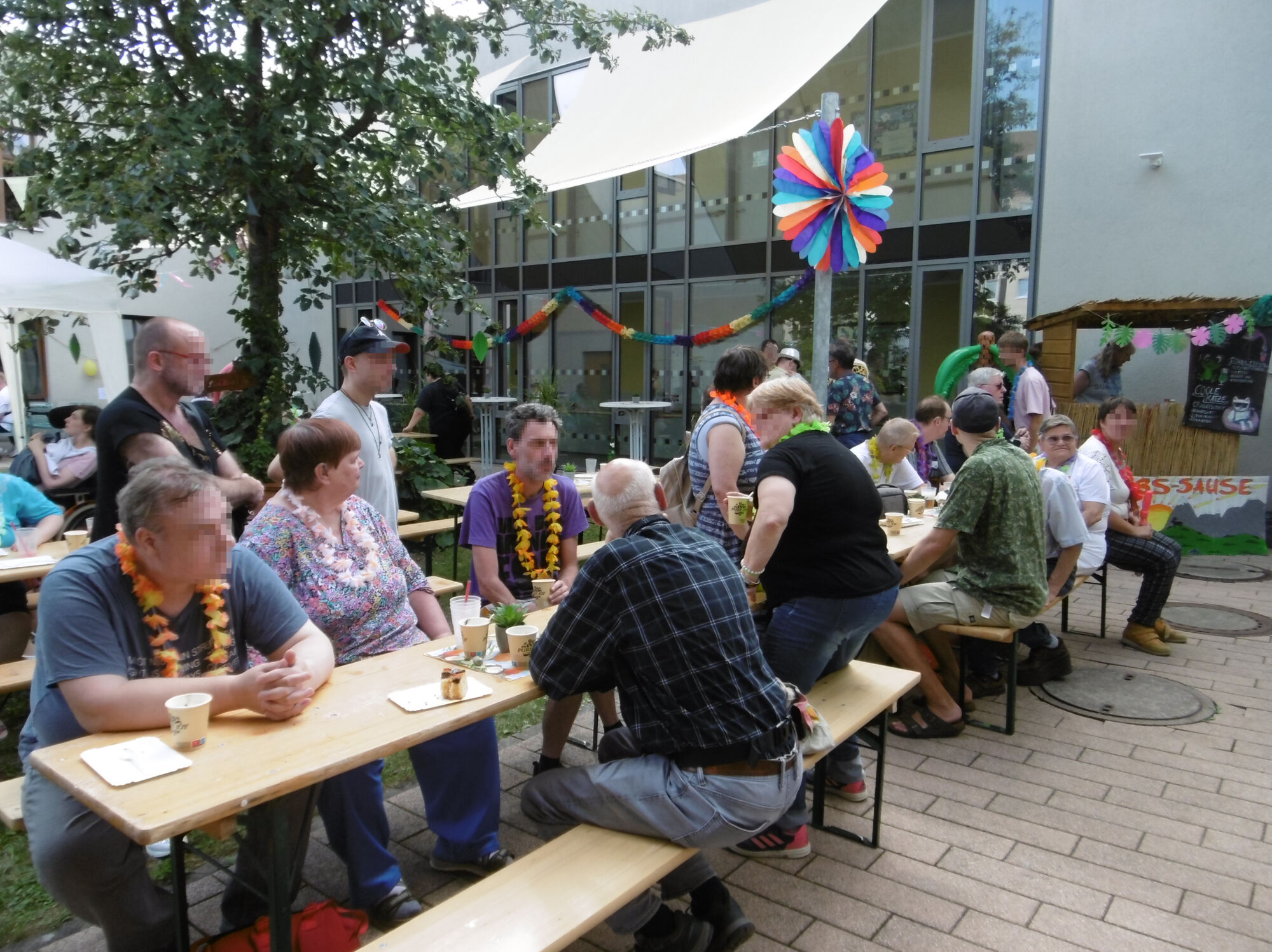 Viele Menschen sitzen auf Bierbänken in einem geschmückten Innenhof