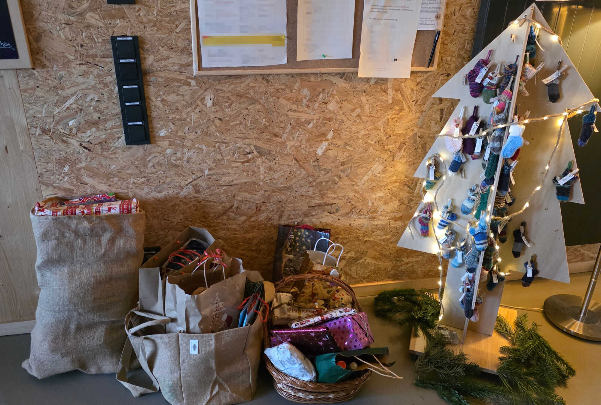 Ein Holzweihnachtsbaum, an dem Geschenke h&auml;ngen. Daneben Jutebeutel mit weiteren Geschenken