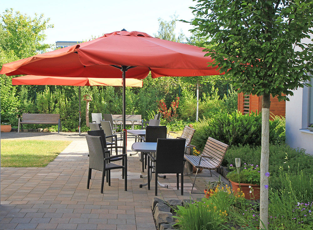 Ein bepflanzter Garten mit Tischen, Stühlen und Sonnenschirmen.