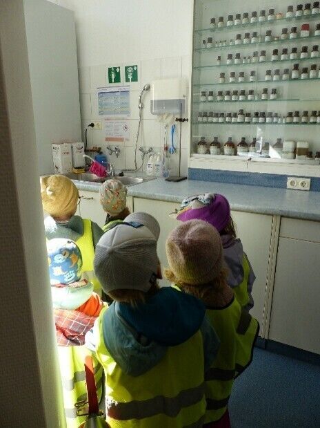 Kinder stehen in einer Apotheke vor einem gro&szlig;en Schrank mit Gl&auml;sern und Tuben
