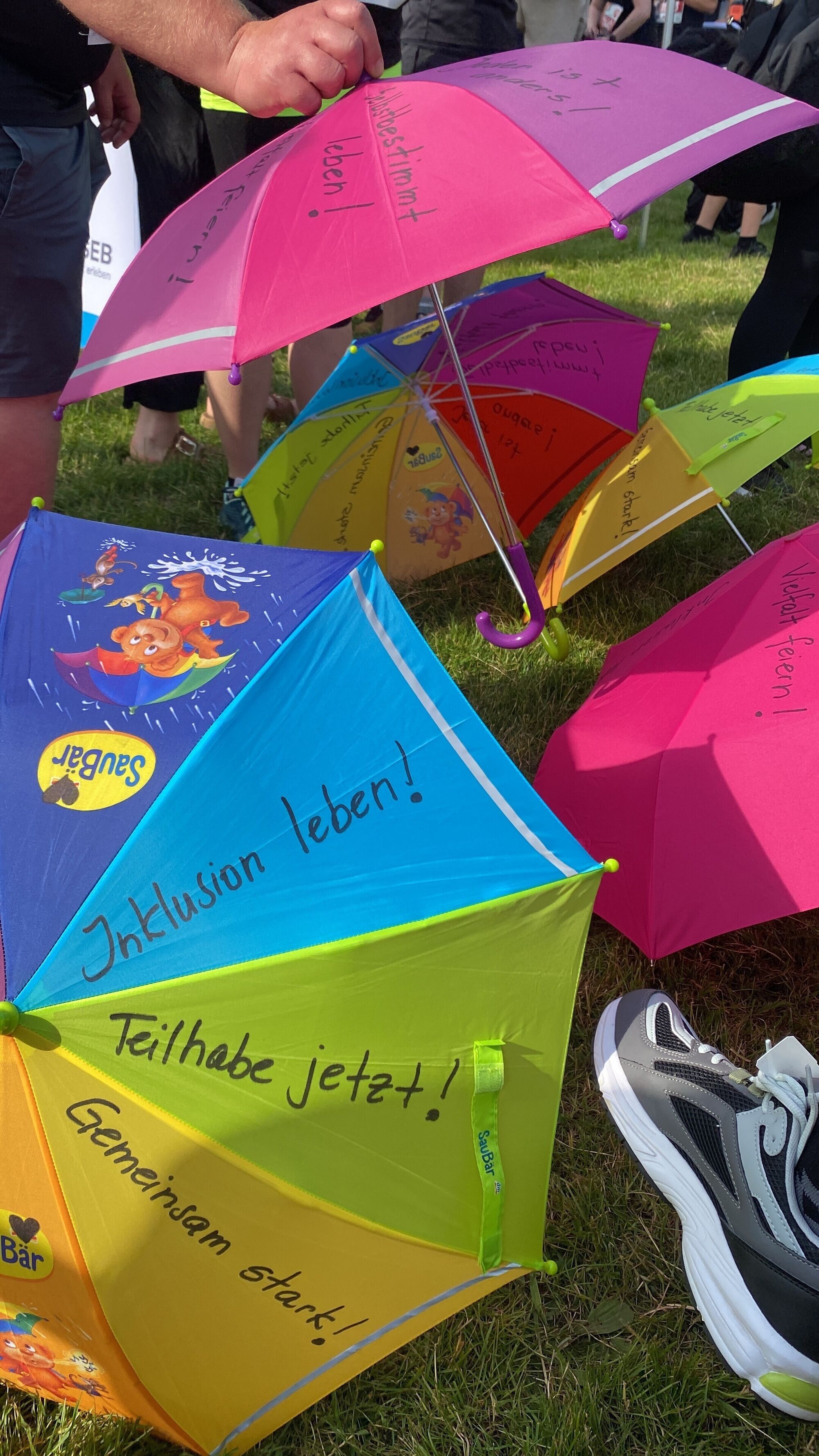 bunte Regenschirme mit Aufschriften wie "Teilhabe jetzt", "Inklusion", Gemeinsam stark"