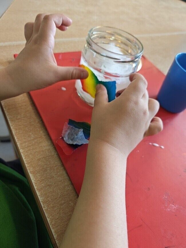 Kinderhänd kleben ein buntes Papier auf ein Schraubglas