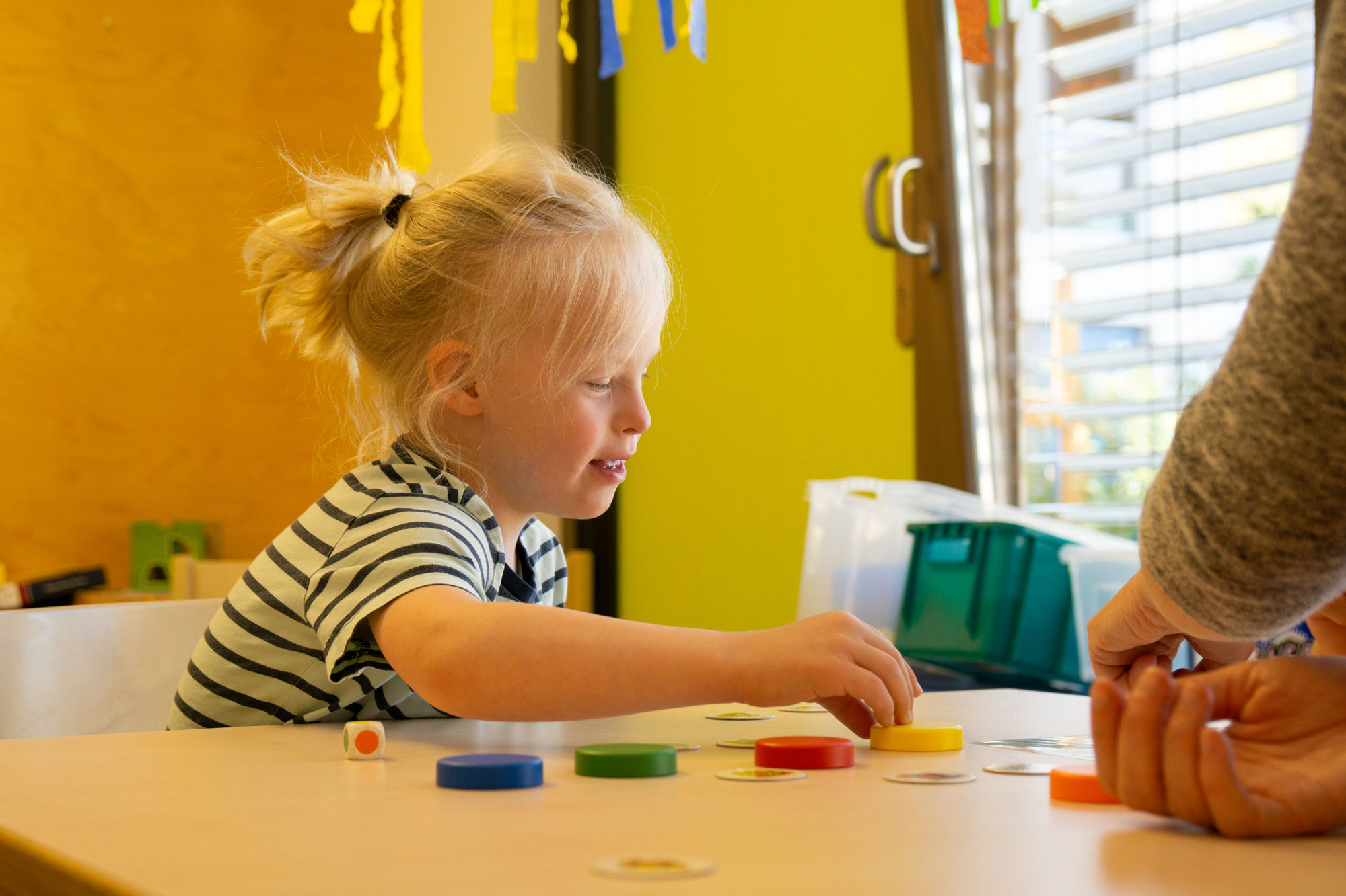 Ein Junge sitzt an einem Tisch mit bunten Holzplättchen und Bilderkarten.