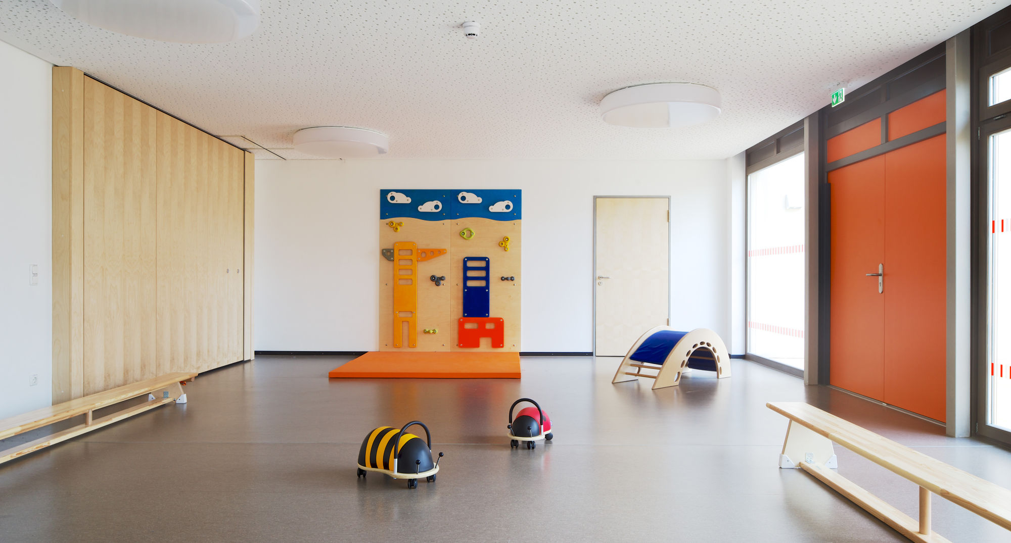 Ein großer Sportraum mit Matten, Sprossenwand und langen Bänken am Rand.