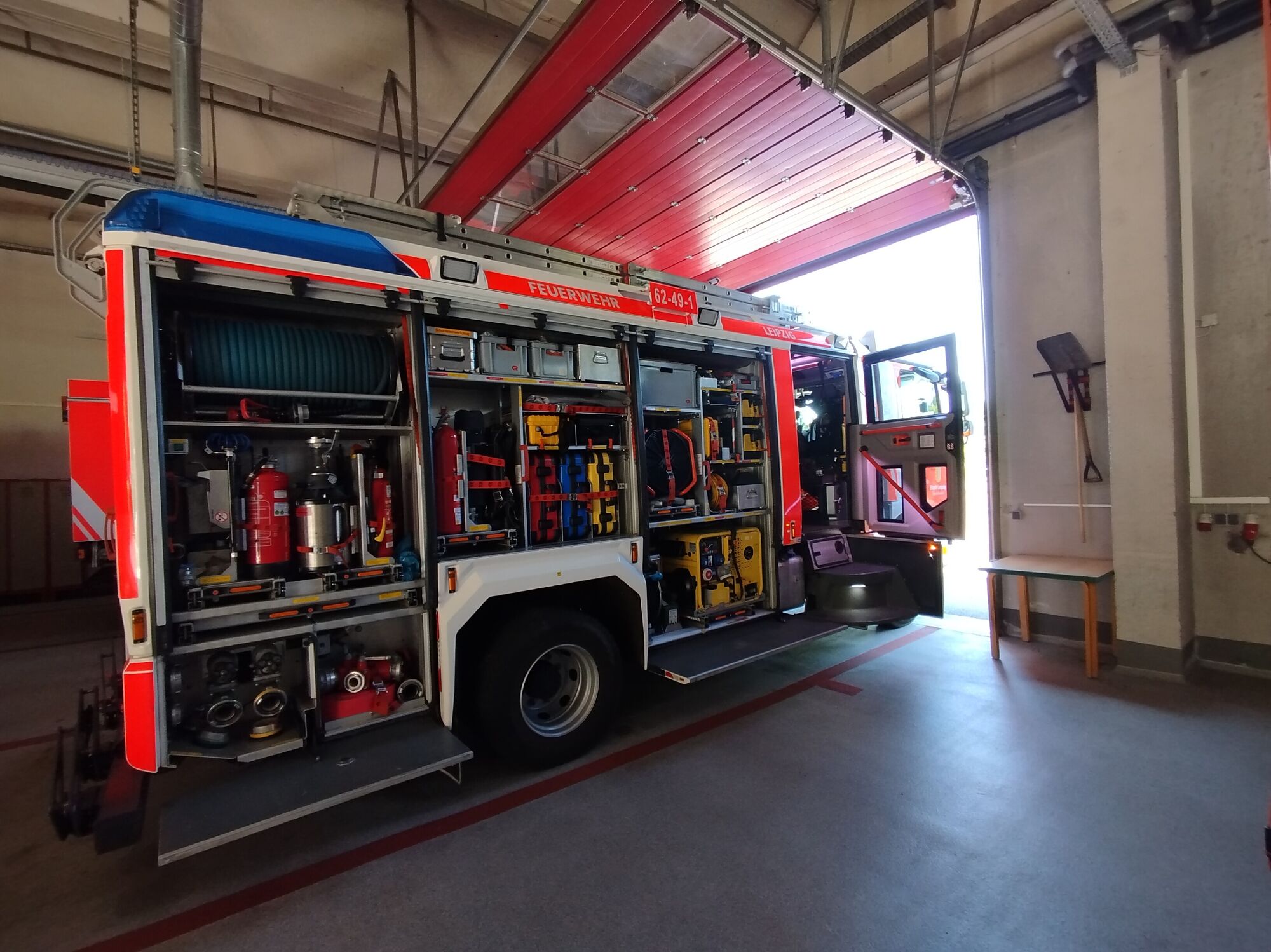 Eine gro&szlig;e feuerwehr in einer Halle mit ge&ouml;ffneter Seite. Werkzeuge und Equipment sind zu sehen.