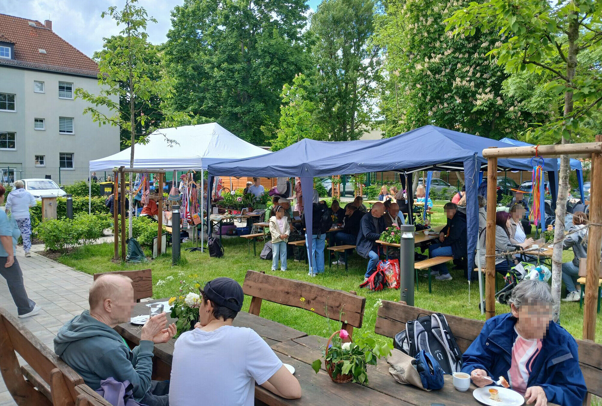 ein Wiese hinter dem Haus mit Pavillons, Sitzb&auml;nken, sch&ouml;ner Deko und vielen Menschen bei Sonnenschein