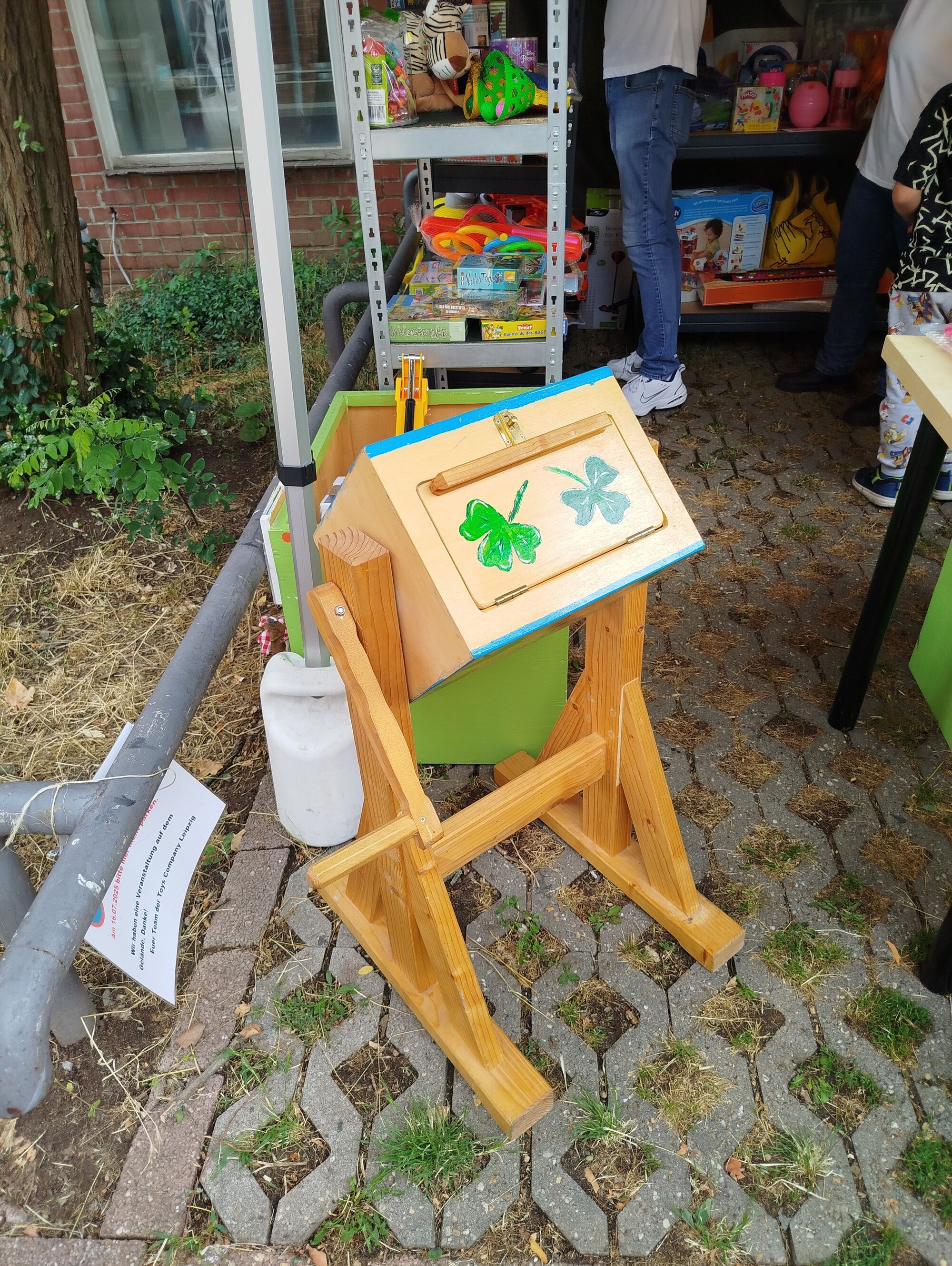 Ein Regal mit vielen Spielgeräten, davor eine Holzkiste mit zwei Kleeblättern darauf
