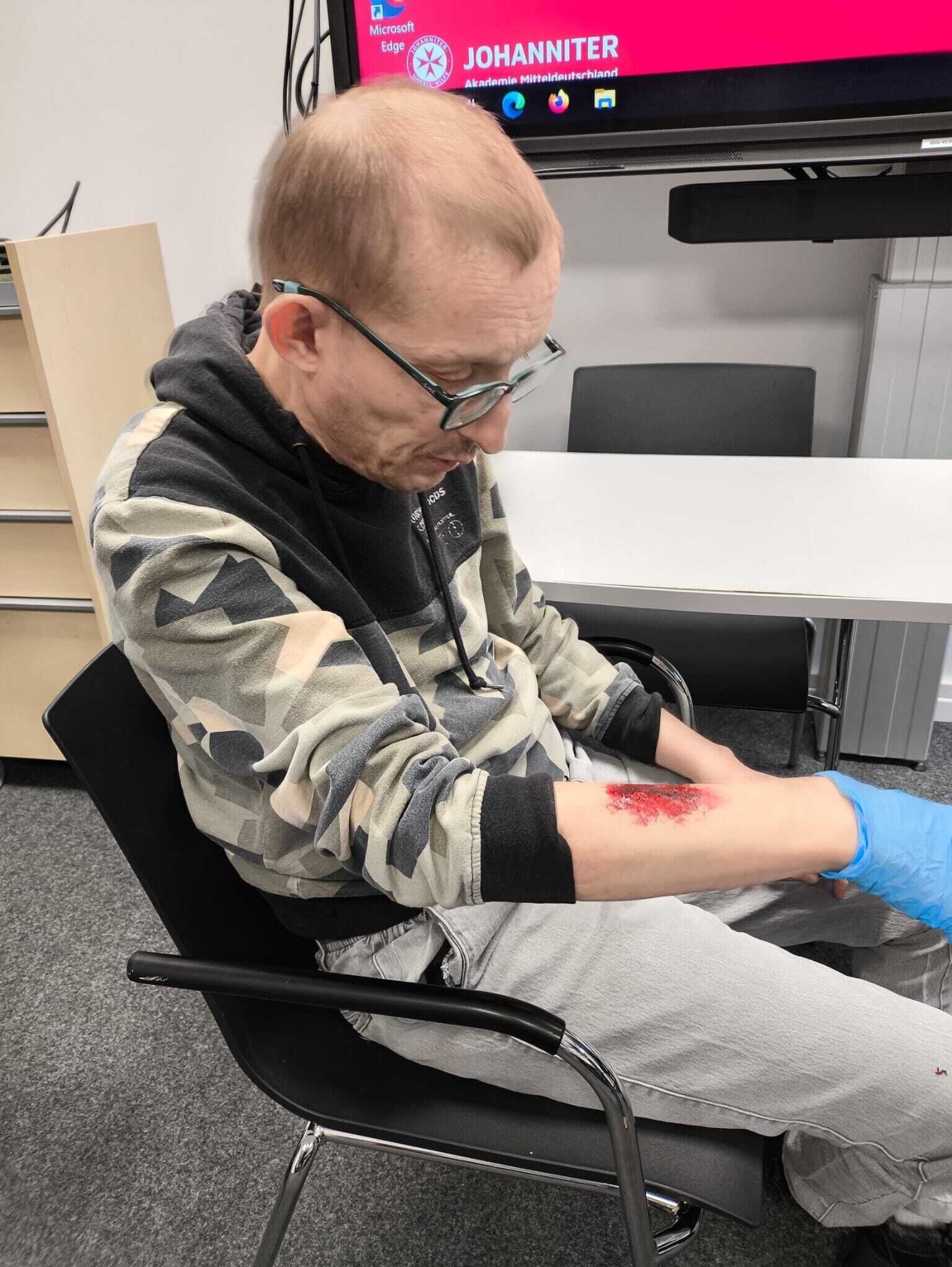 Ein Mann mit einer aufgeklebten Wunde sitzt auf einem Stuhl