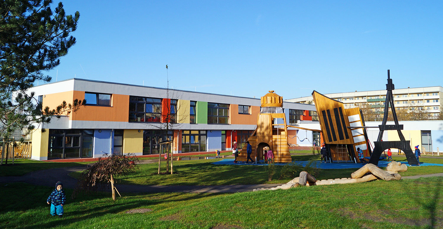 Der große-Kita-Garten mit Wiese, Sandkästen und großen Klettertürmen.