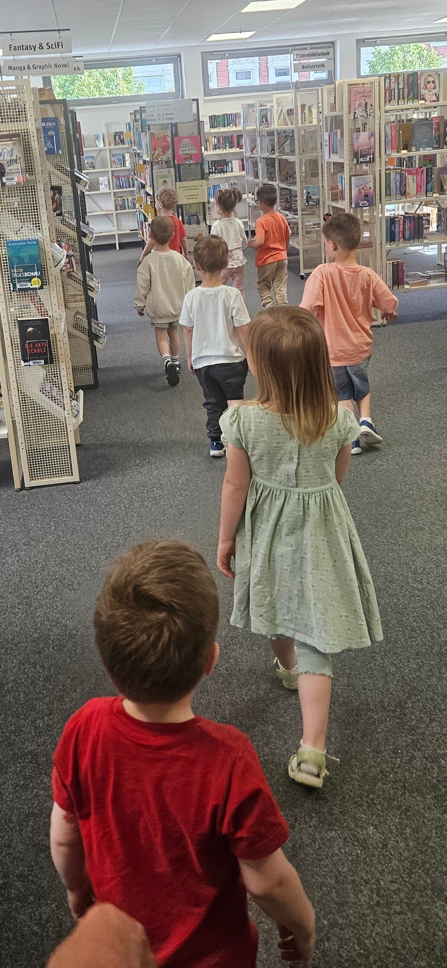 Kinder laufen durch die G&auml;nge mit B&uuml;cherregalen