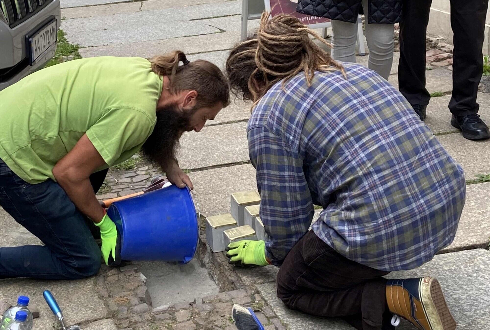Zwei M&auml;nner verlegen die Stolpersteine in einem Gehweg