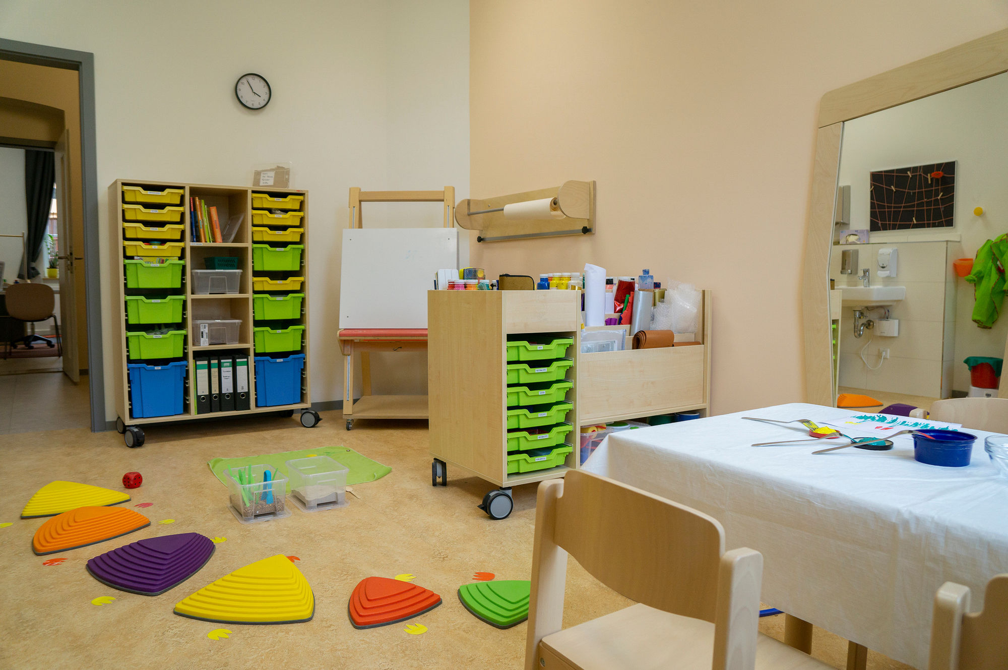 ein Therapieraum mit Tisch, Stühlen, Staffelei,.Farbdosen, Papierrollen und weiteren Therapiematerialien
