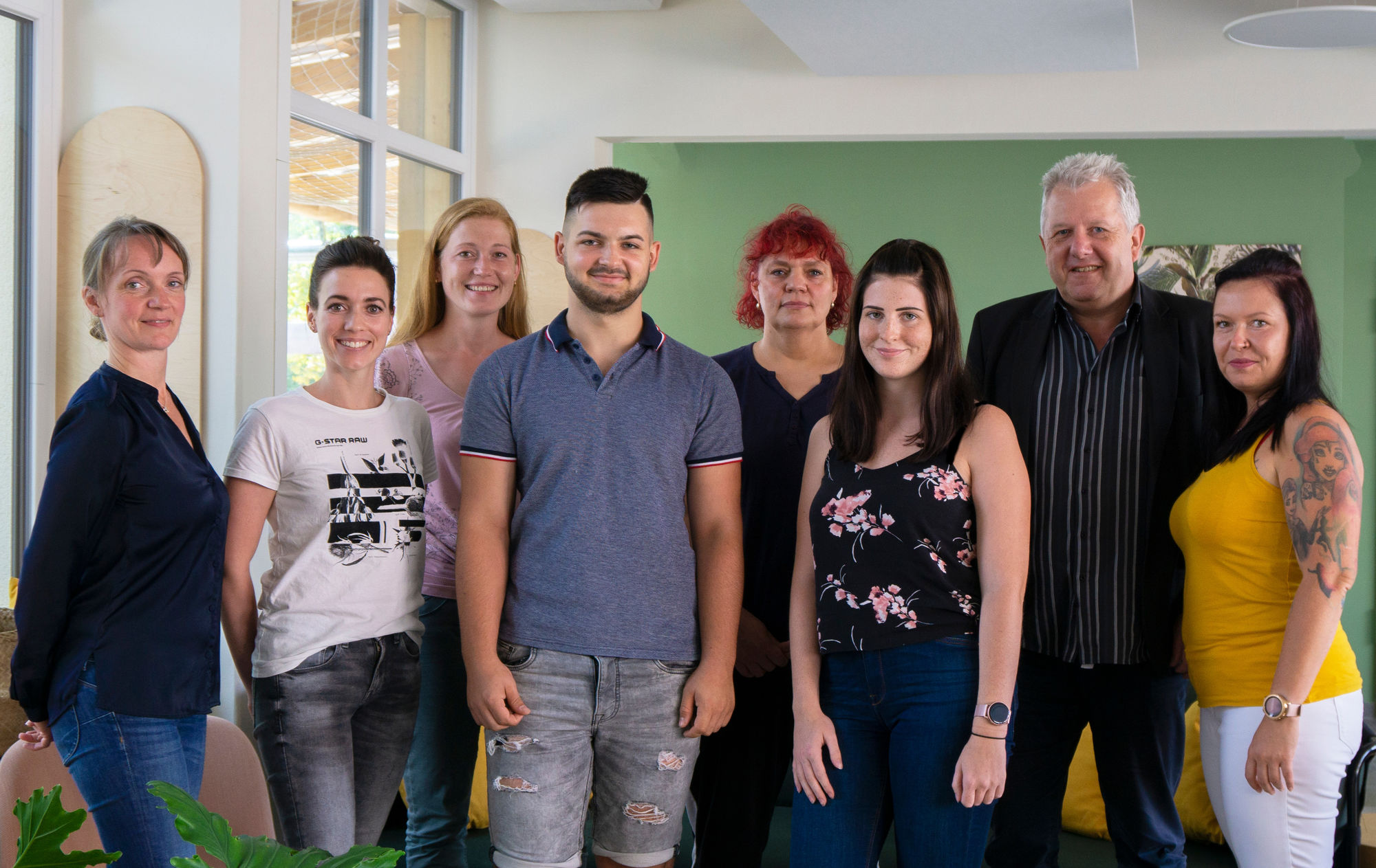 Acht Menschen stehen gemeinsam in einem Raum und lächeln in die Kamera.