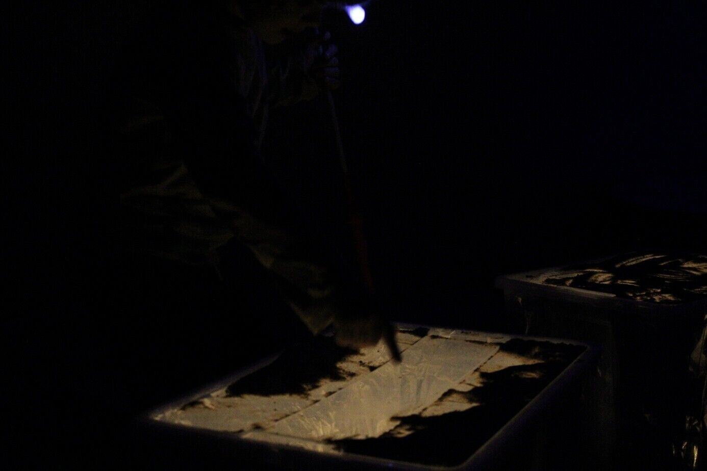 ein sehr dunkler Raum mit Kisten, deren obere Seite hinterleuchtet ist. Darauf kann man in Sand malen und so durch Licht und Schatten Bilder erzeugen.