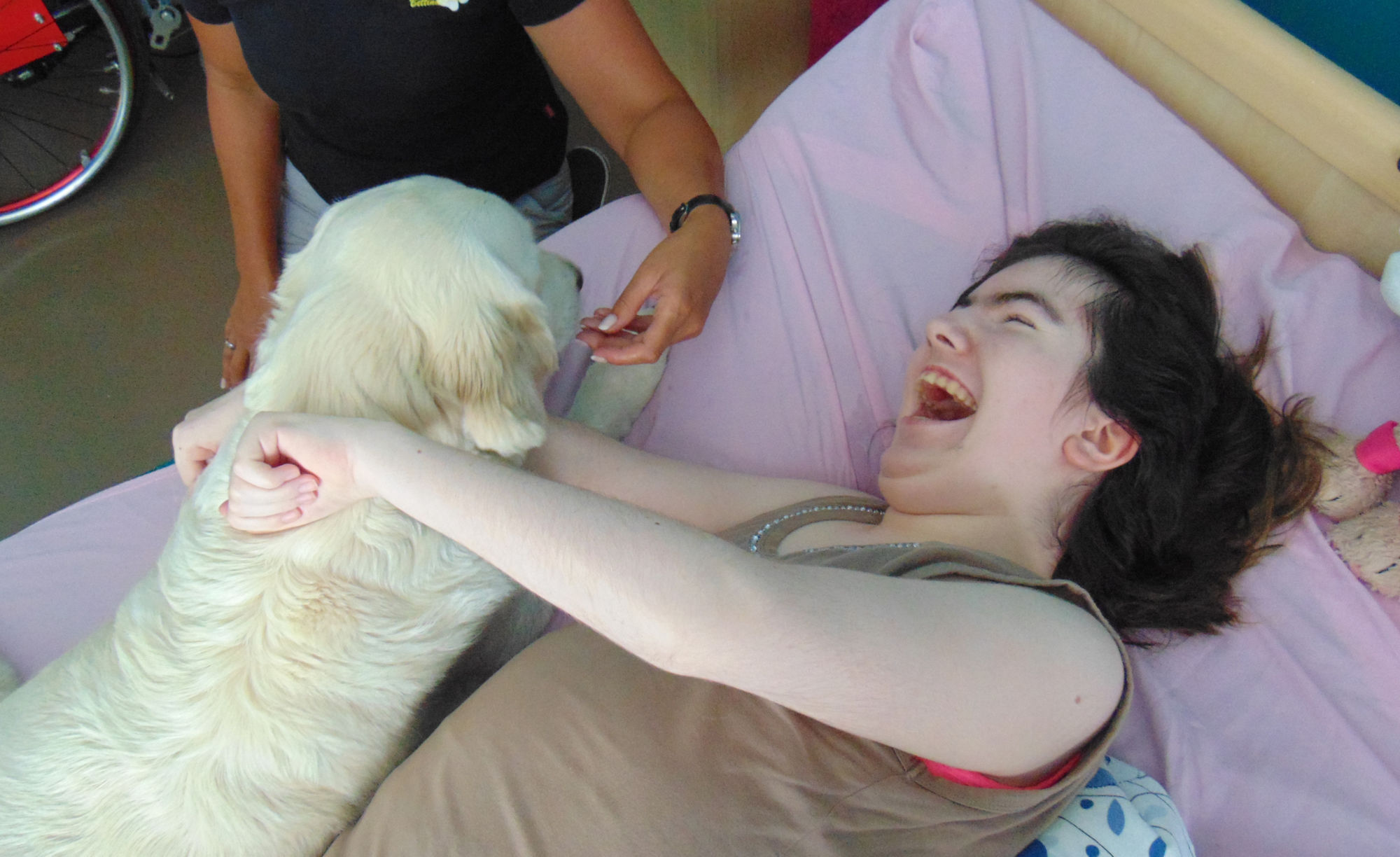 Ein Frau liegt lachend in einem Bett. Neben ihr ist ein weißer Hund.