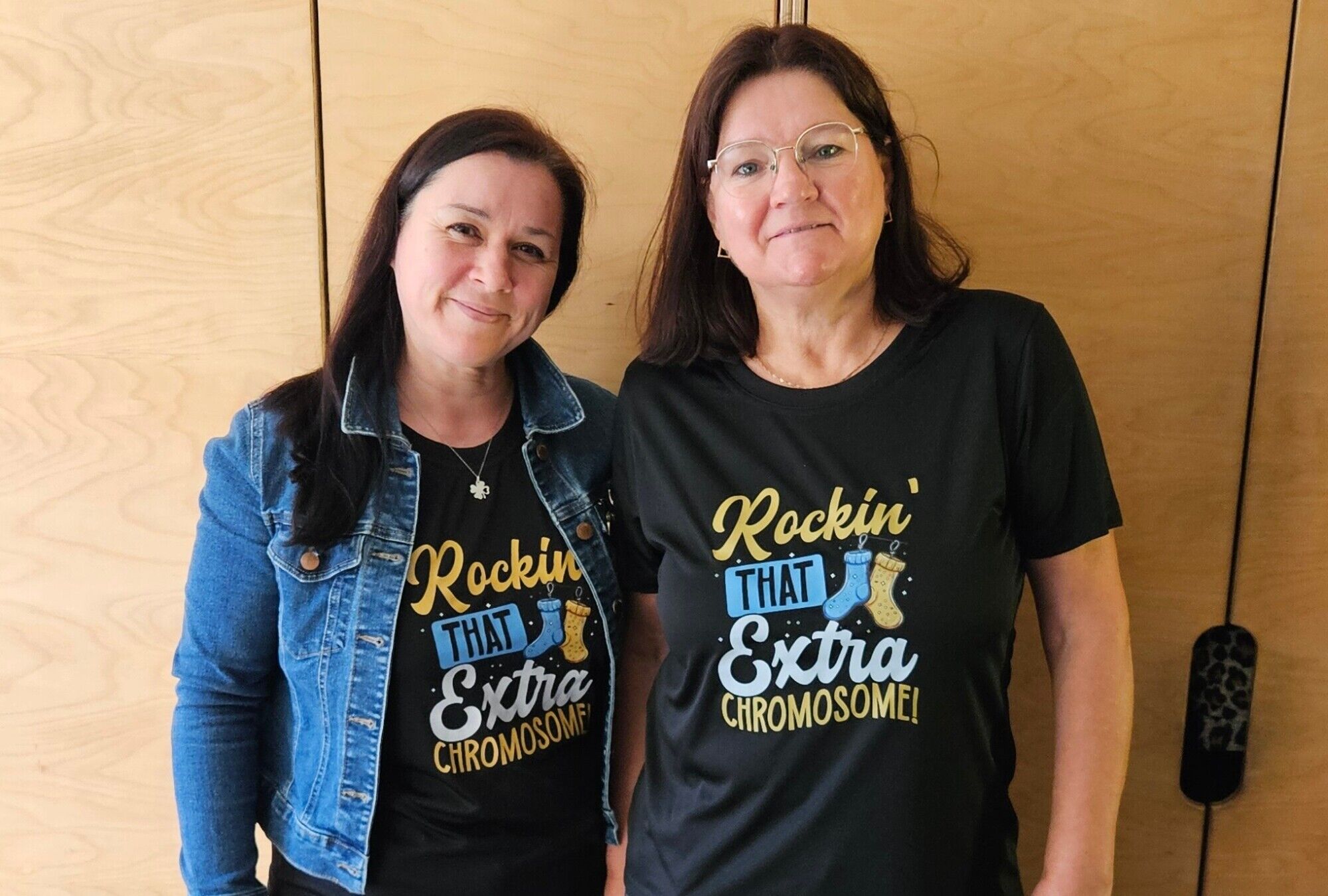 Zwei Frauen mit einheitlichen T-Shirts mit dem Text "rockin that extra chromosome" und bunten Socken an den F&uuml;&szlig;en