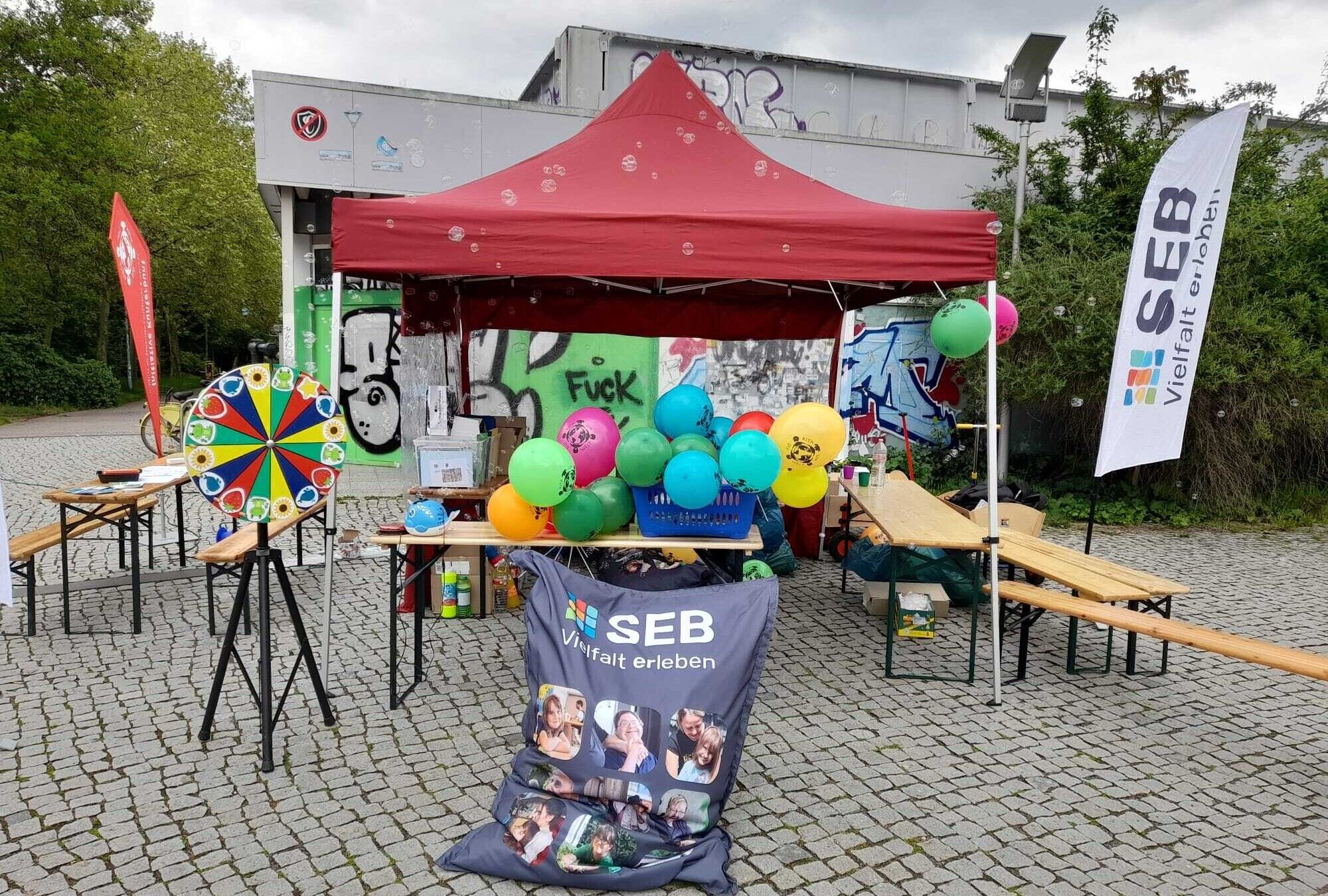 Ein Pavillon mit Bierb&auml;nken, einem Gl&uuml;cksrad, Luftballons mit Kita-Logo und Werbefahne vom SEB