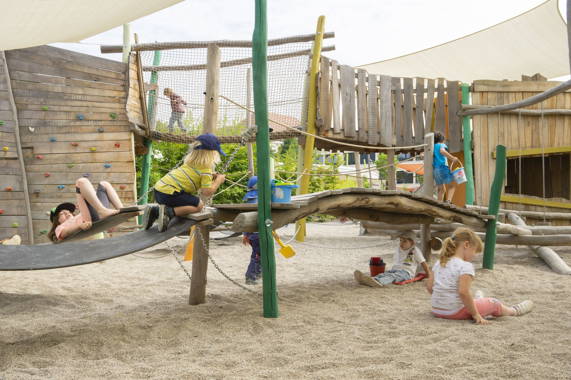 Kinder spielen im Sand und auf einem Kletterbereich mit schwarzen Schwungmatten