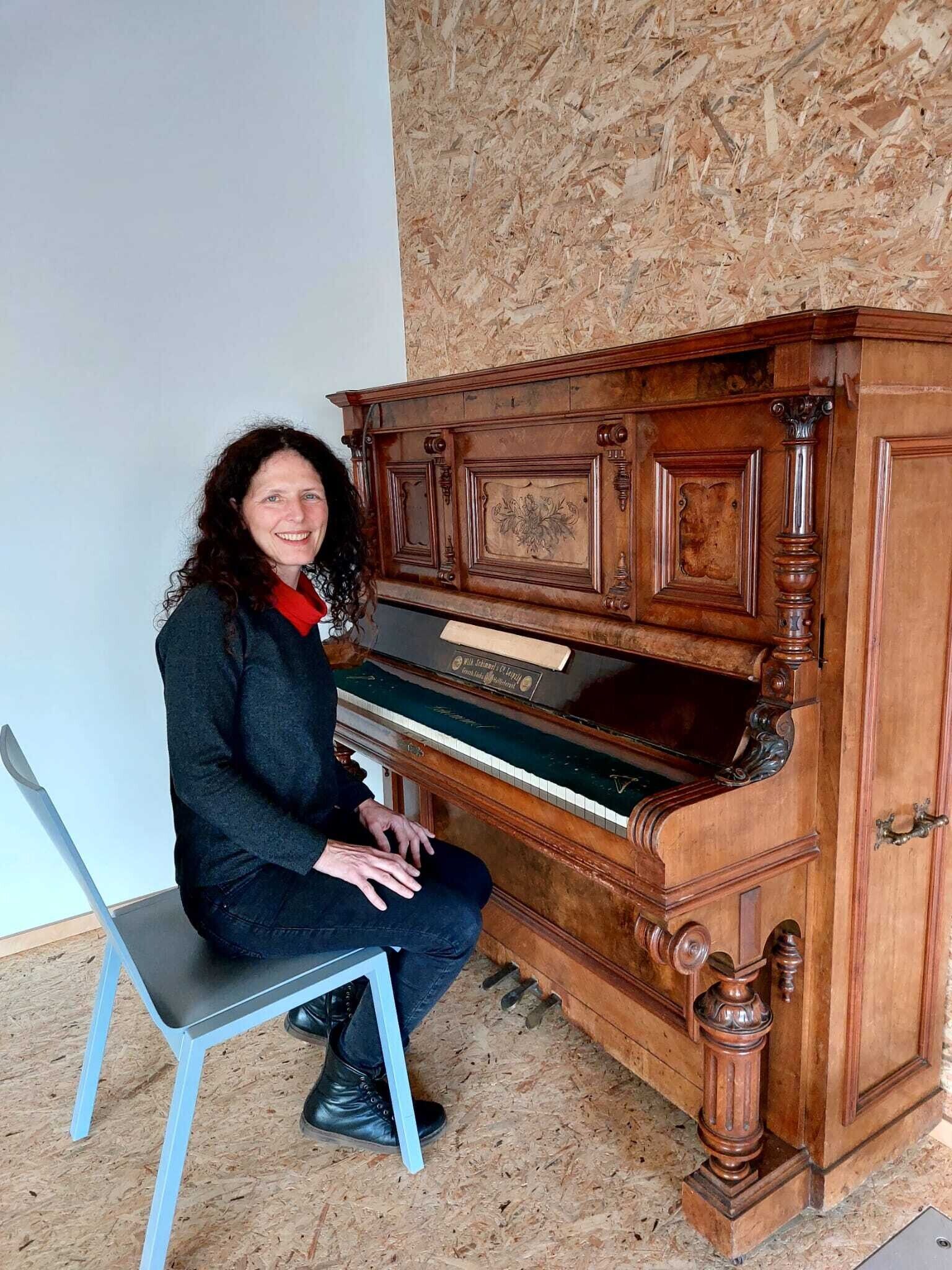 Eine Frau sitzt an einem Klavier und lacht in die Kamera