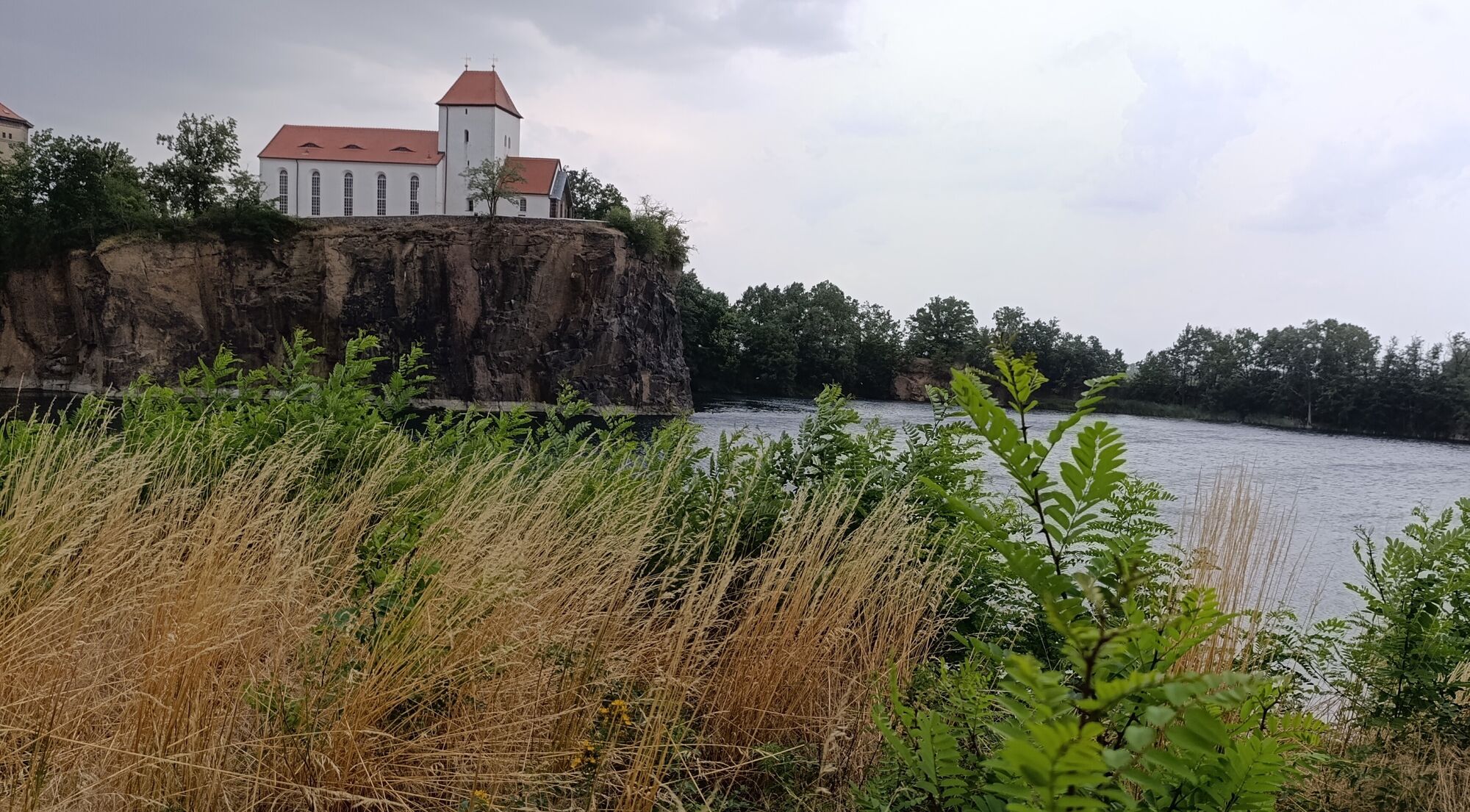 Der Steinbruch Beucha. Eine wei&szlig;e Kirche auf einer kleinen Klippa. Davor der See.