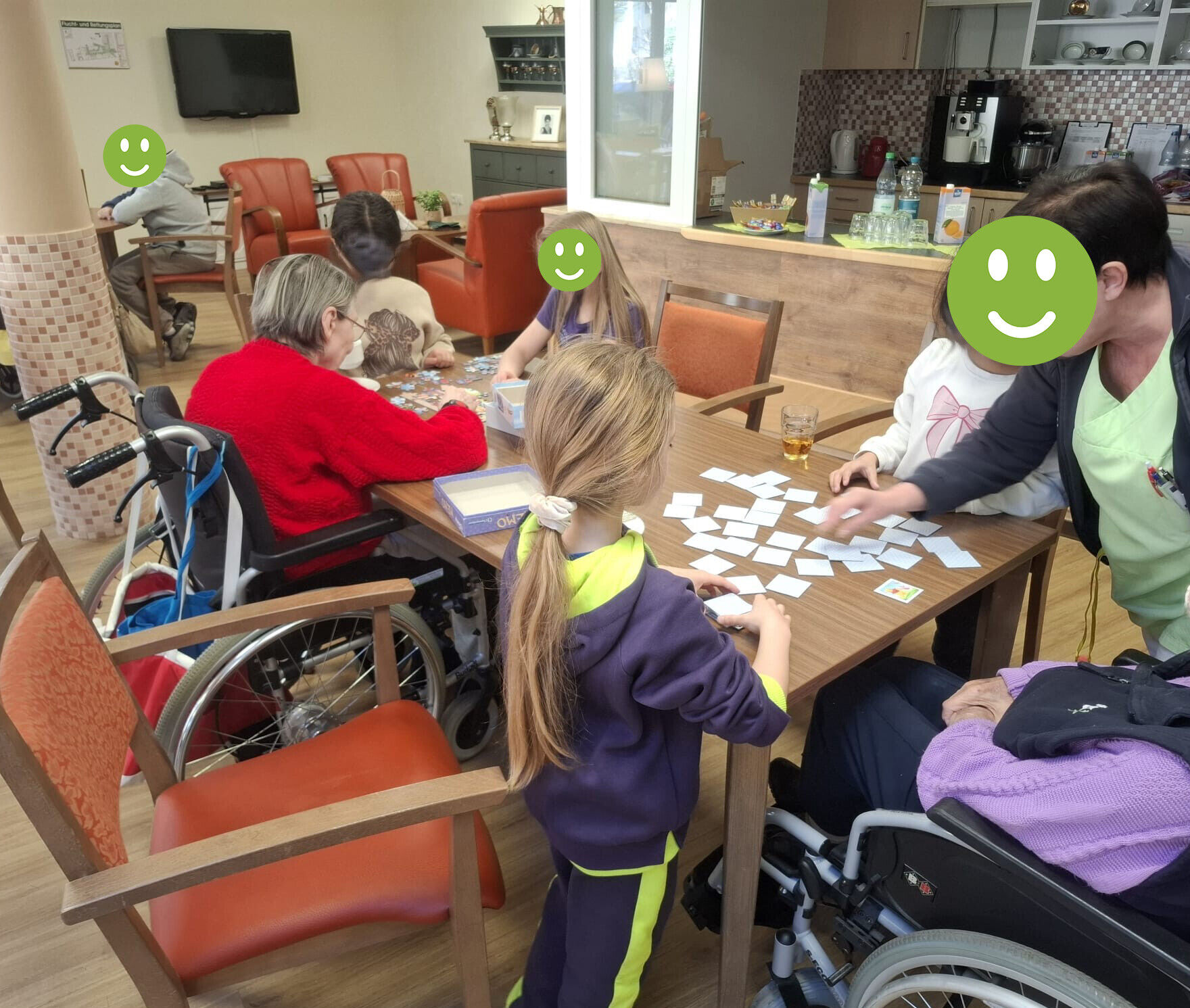 Kinder und&auml;ltere Menschen sitzen an einem gro&szlig;en Tisch und spielen Spiele