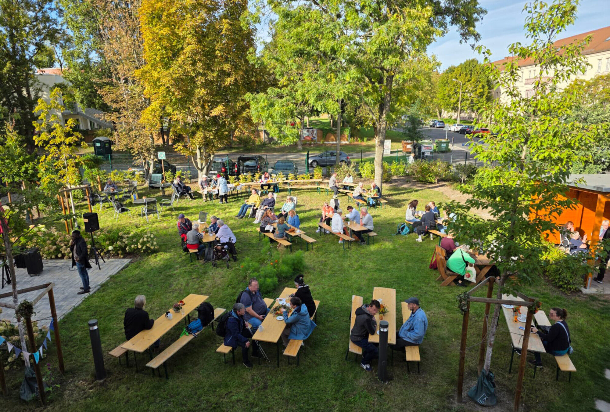 Viele Menschen sitzen in einem gro&szlig;en Garten bei Sonnenschein