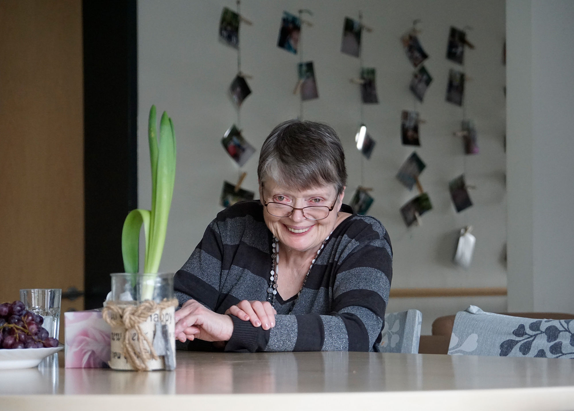 Eine Frau sitzt lachend an einem Tisch mit frischen Blumen.