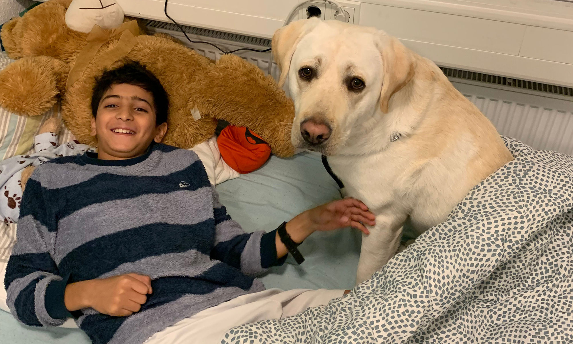 © SEB Leipzig Ein Kind liegt lachend auf einem Bett, daneben sitzt ein Hund.