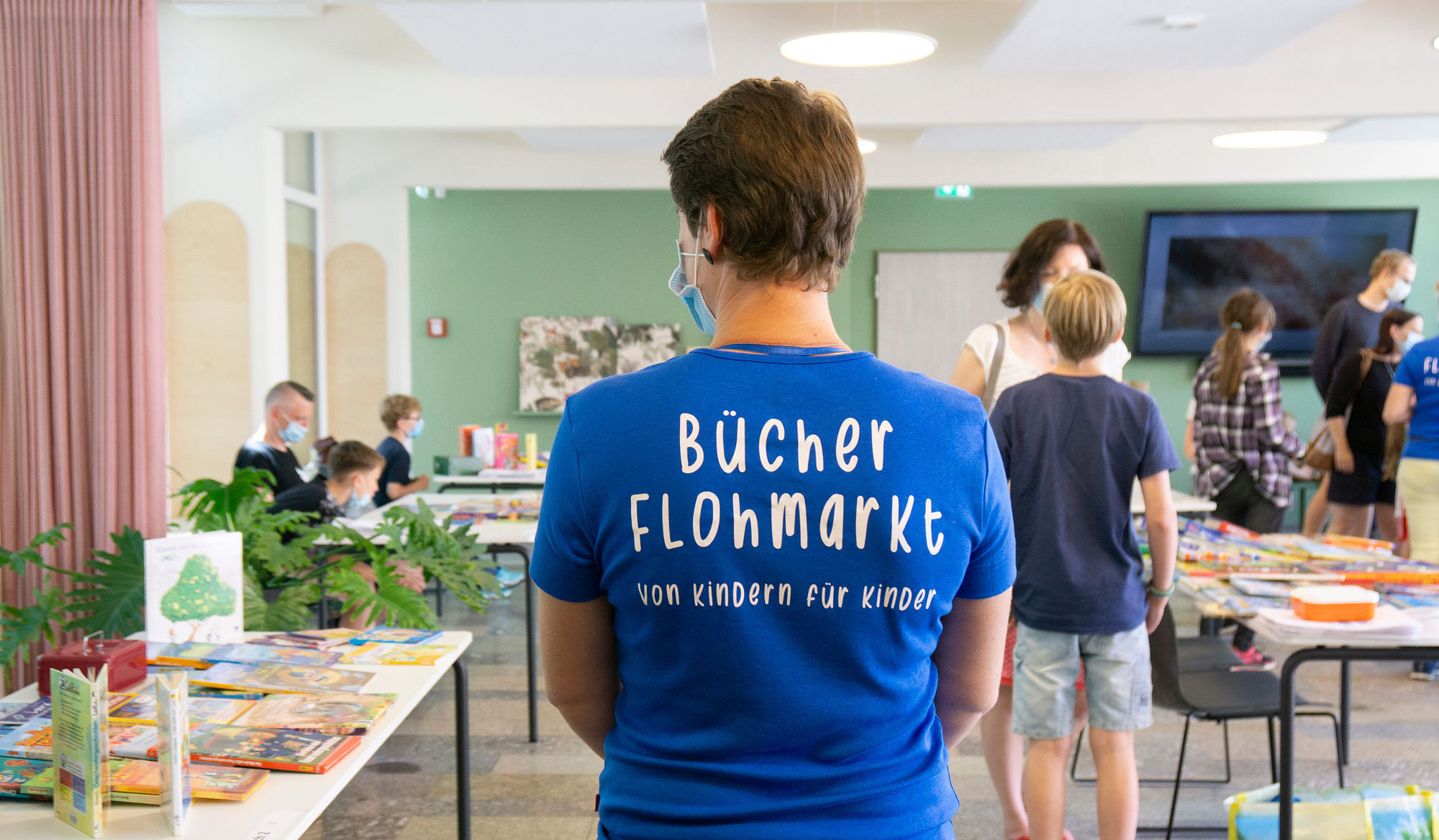 Ein Frau hat ein blaues T-Shirt mit der Aufschrift Bücherflohmarkt an
