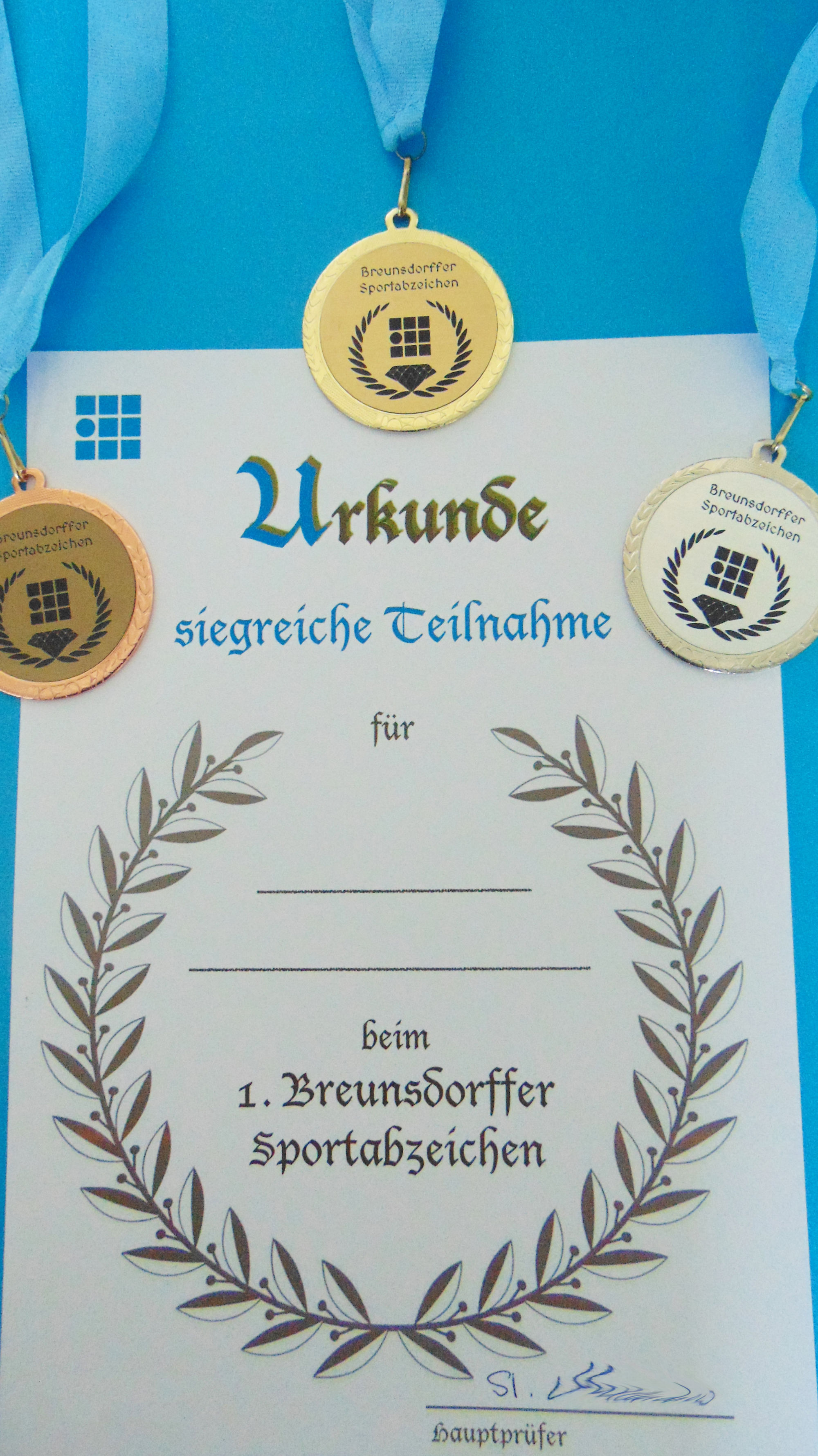 Ein Urkunde und drei Medaillen mit der Aufschrift "Breunsdorffer Sportabzeichen"