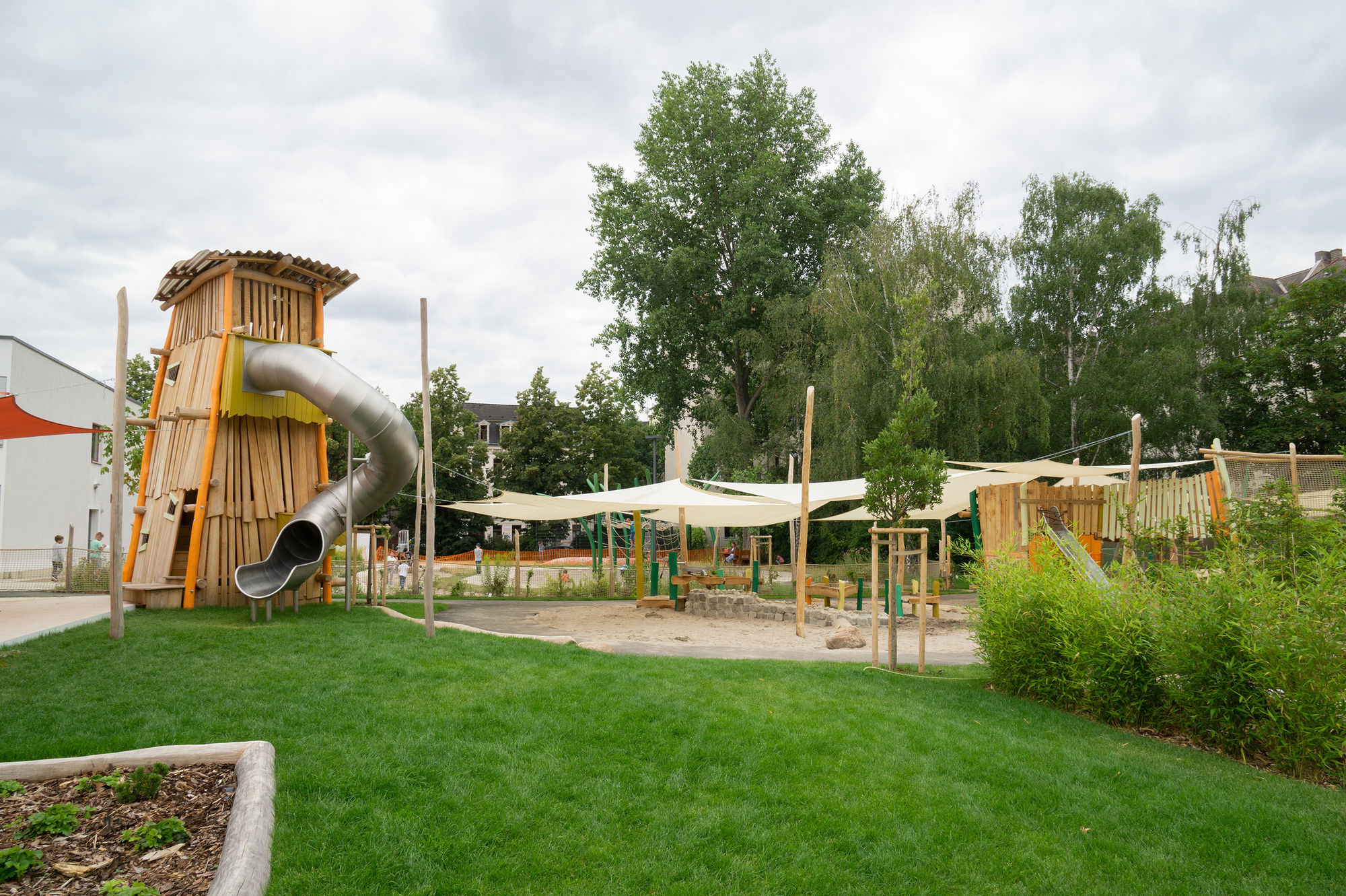 Eine Wiese, ein Sndkastenbereich mit Sonnensegeln und ein großer Rutschenturm
