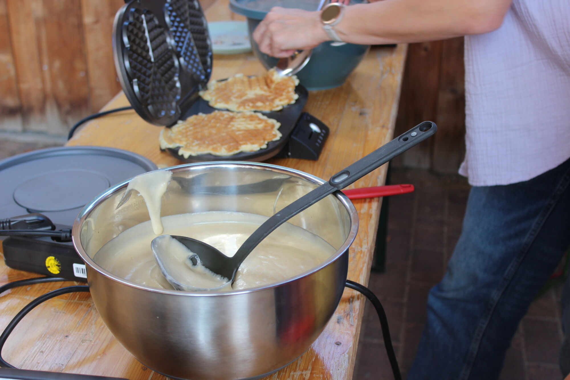 Eine gro&szlig;e Sch&uuml;ssel mit Teig, dahinter ein Waffeleisen mit knusprigen gebackenen Waffeln