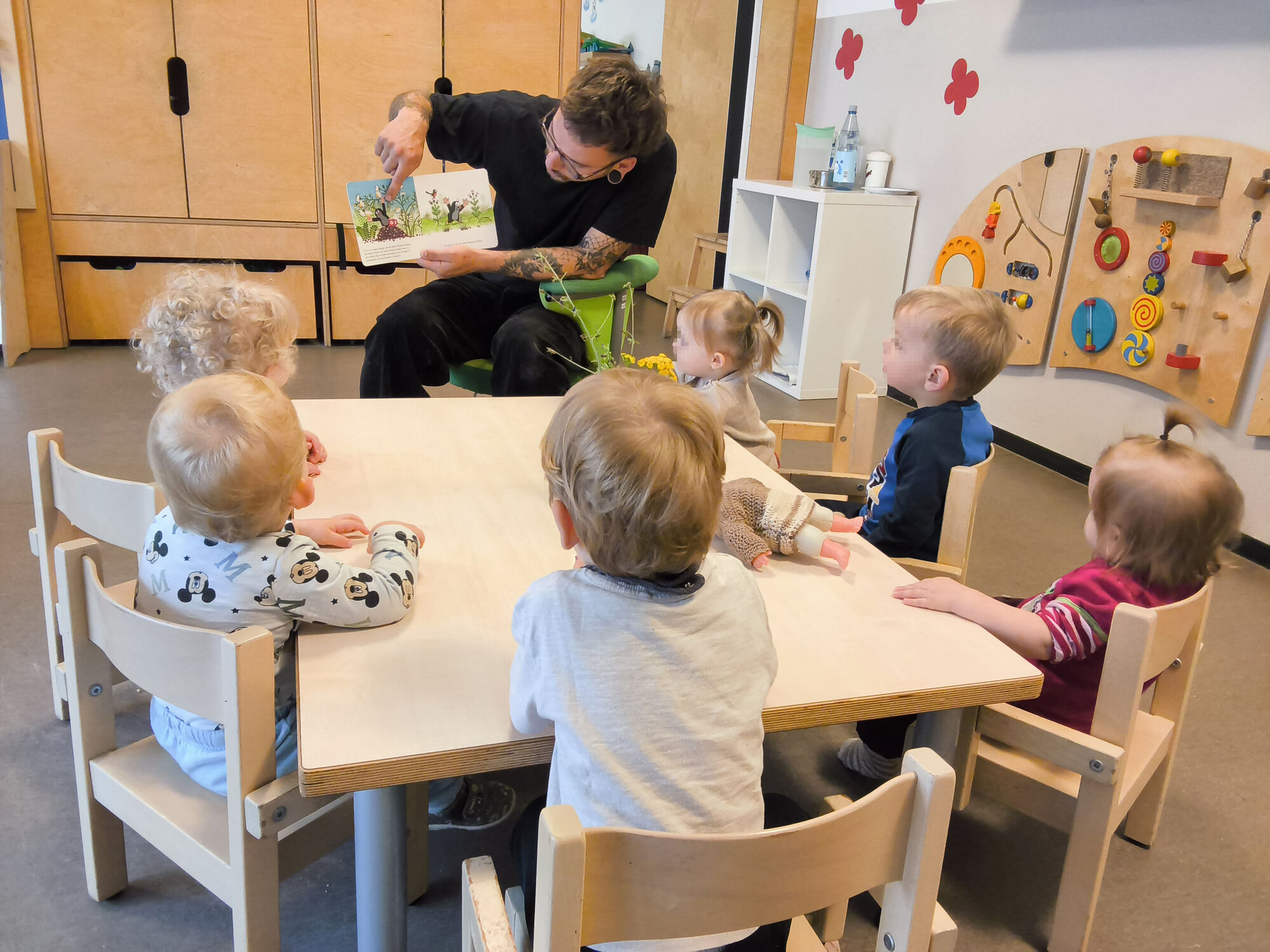 Ein Erzieher zeigt den Kindern Bilder in einem Buch. alle sitzen an einem Tisch.