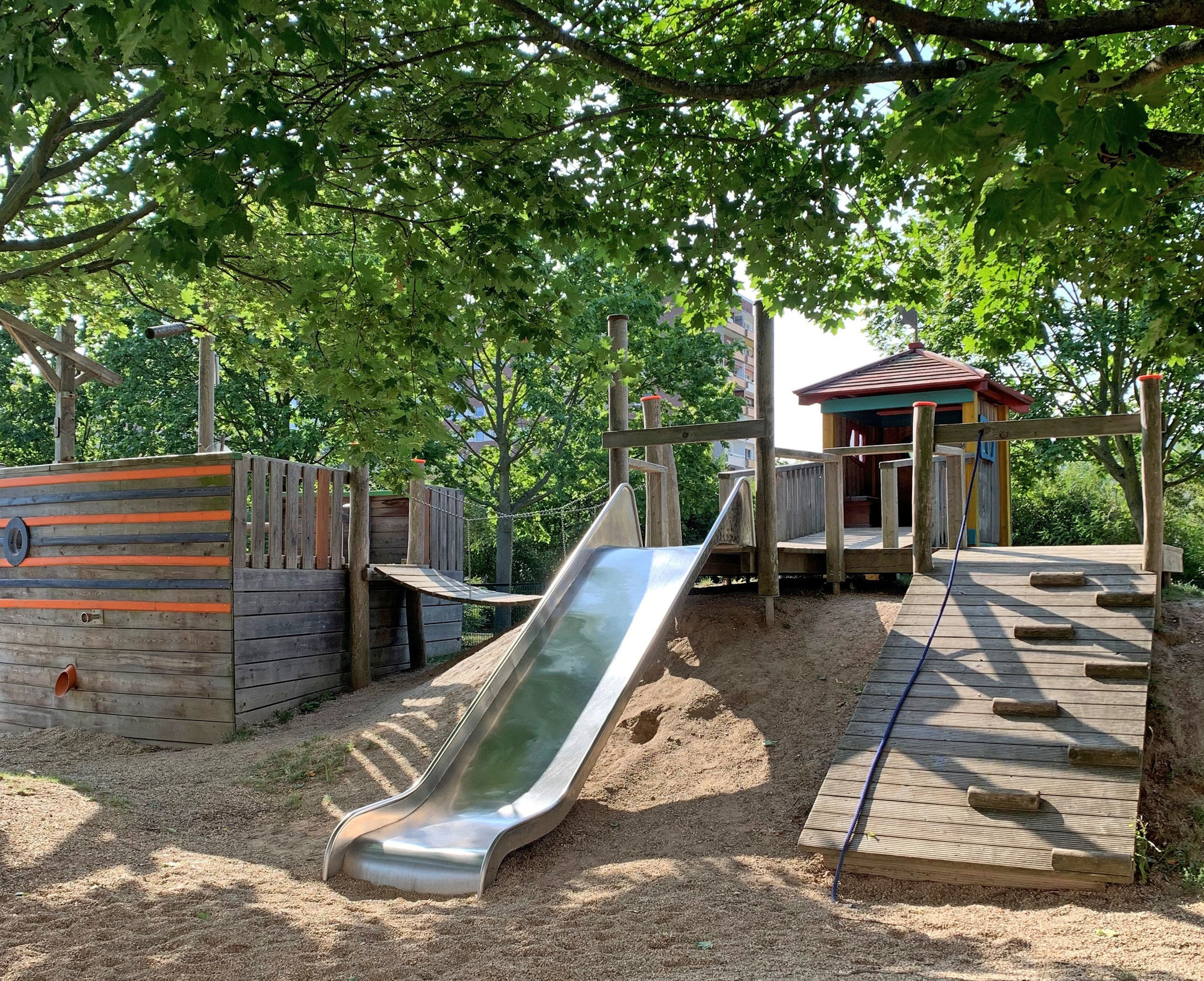 Ein von Bäumen umgebener Kletterbereich mit Rutsche.