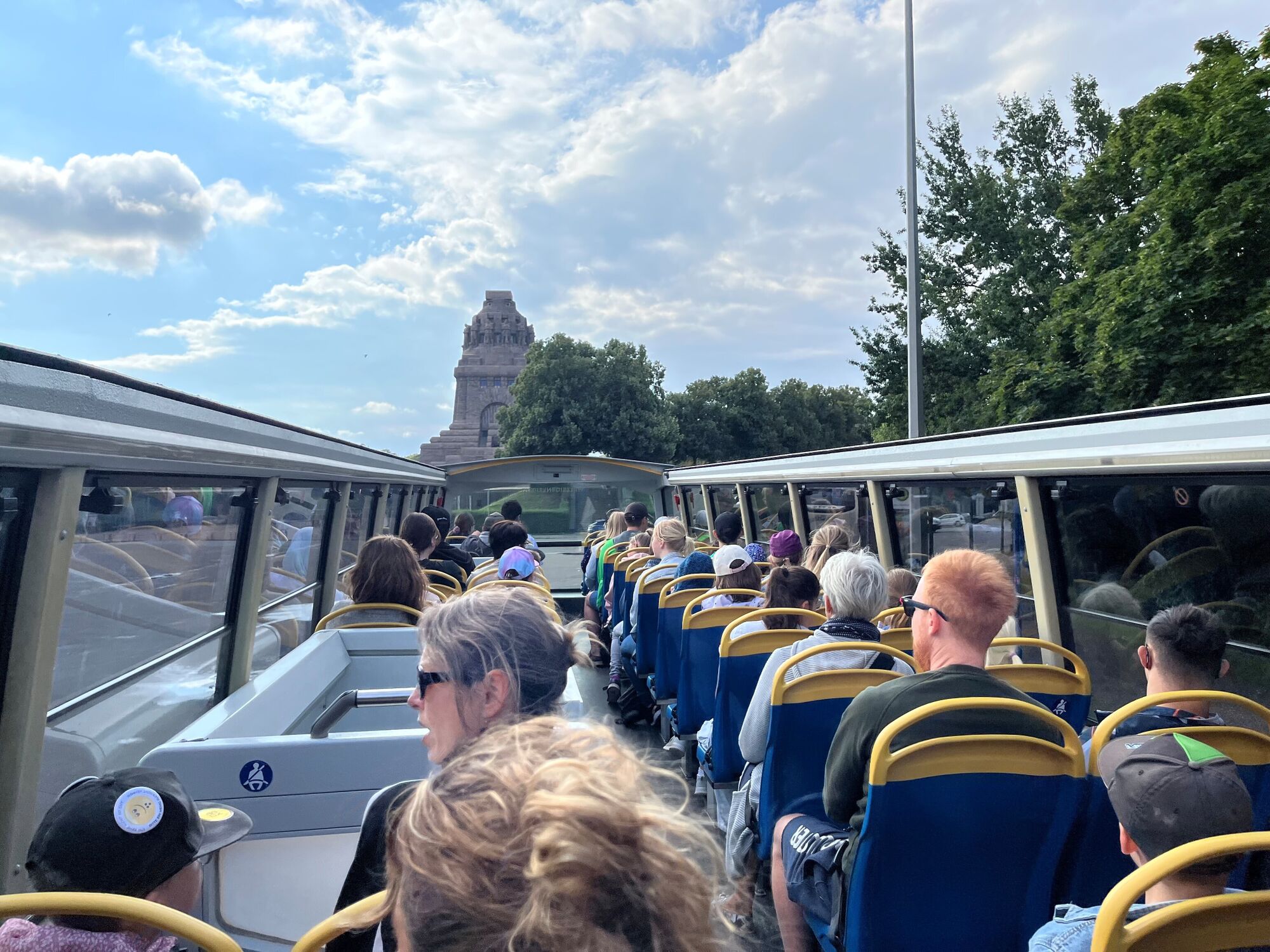 Menschen sitzen im Bus, oben ist kein Dach, das Völkerschlachtdenkmal ist in der ferne zu sehen