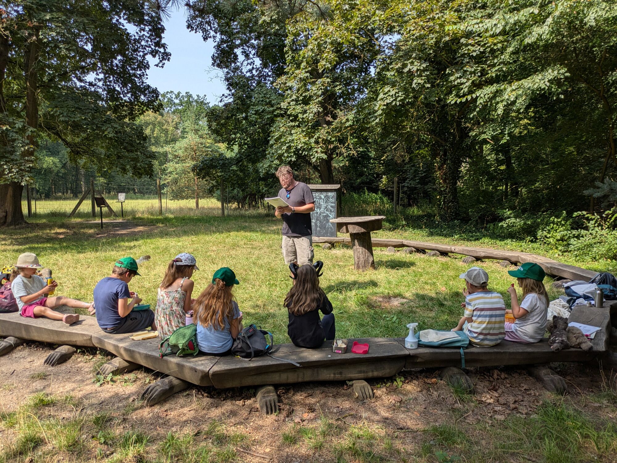 Kinder sitzen auf Holzbalken und h&ouml;ren einem Mann zu