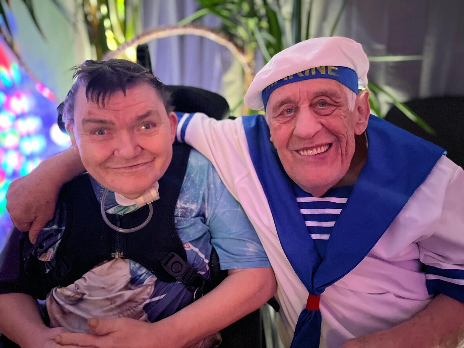 Zwei verkleidete Menschen lachen in die Kamera. Einer legt einen Arm um die Schulter des anderen