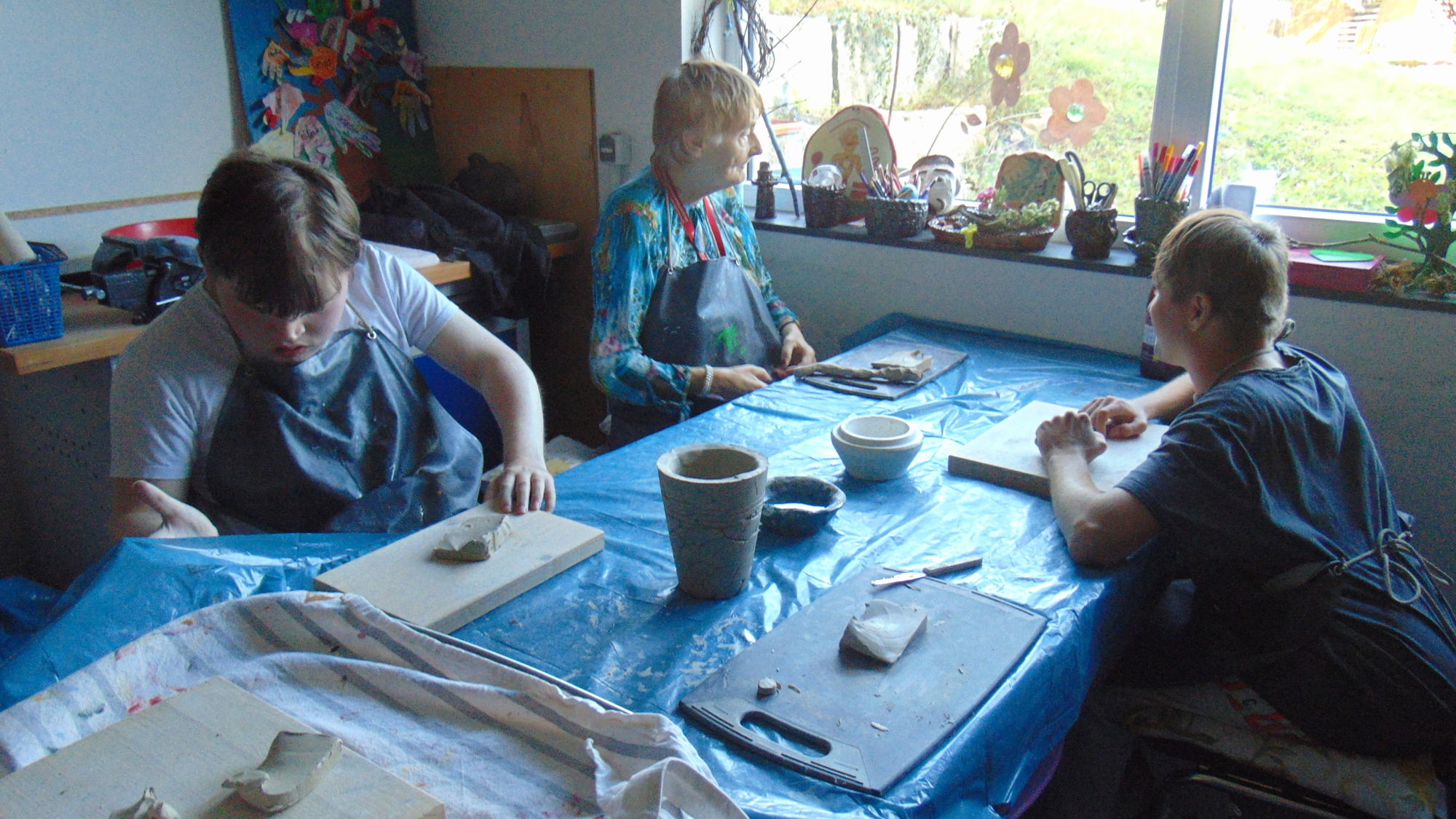 Drei Menschen sitzen an einem Tisch und basteln mit Ton.