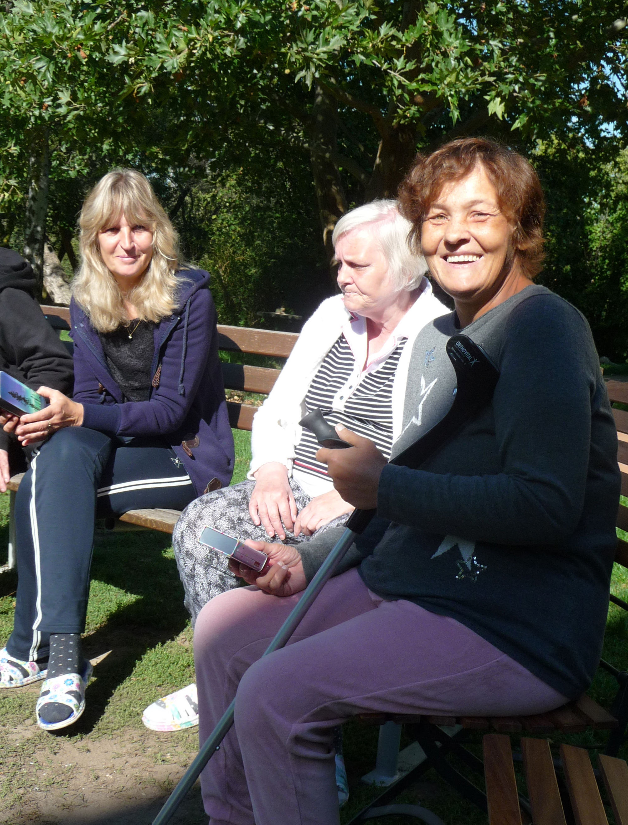 Drei Frauen sitzen auf einer bank in der Sonne.