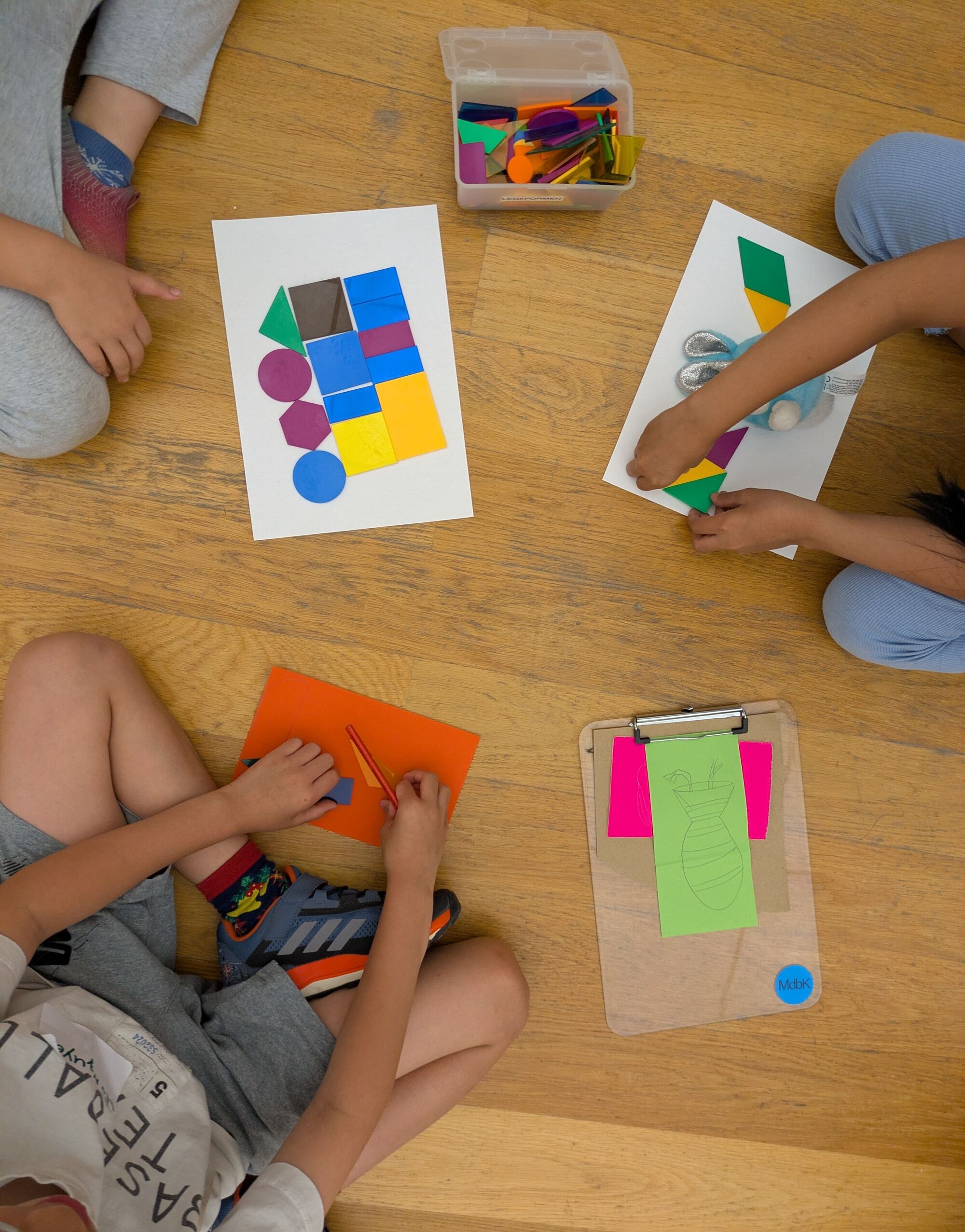 Kinder sitzen auf dem Boden und legenbunte gefaltete geometrische Formen auf wei&szlig;es Papier