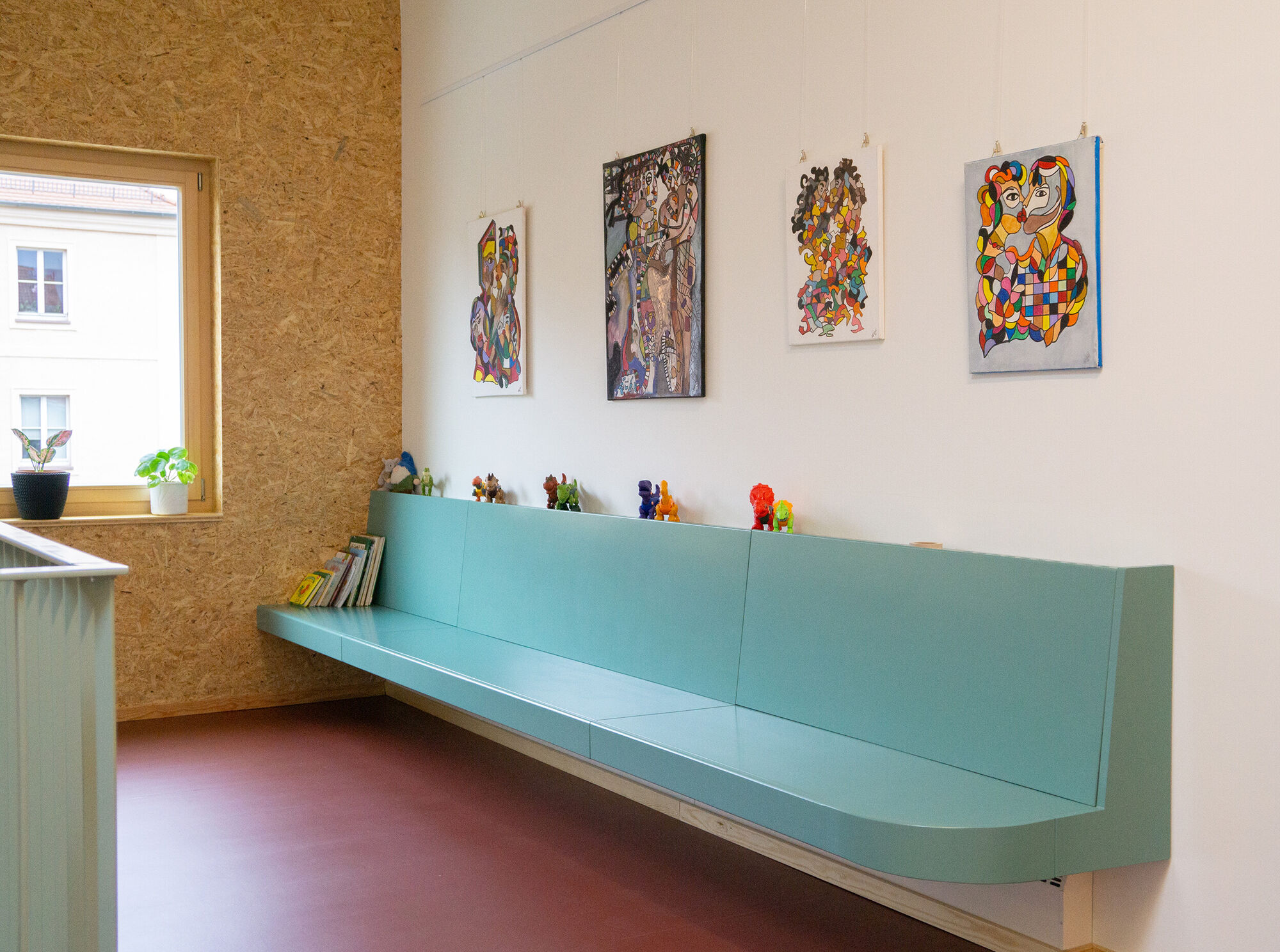 eine türkisfarbene Sitzbank an einer Wand mit bunten Gemälden