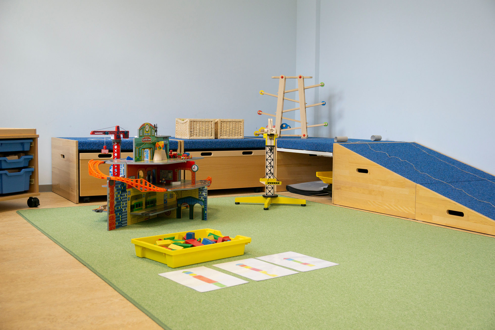 Ein Raum mit grünem teppich, Autospielhaus, Rampen, Murmelbahn und anderen Spielen.