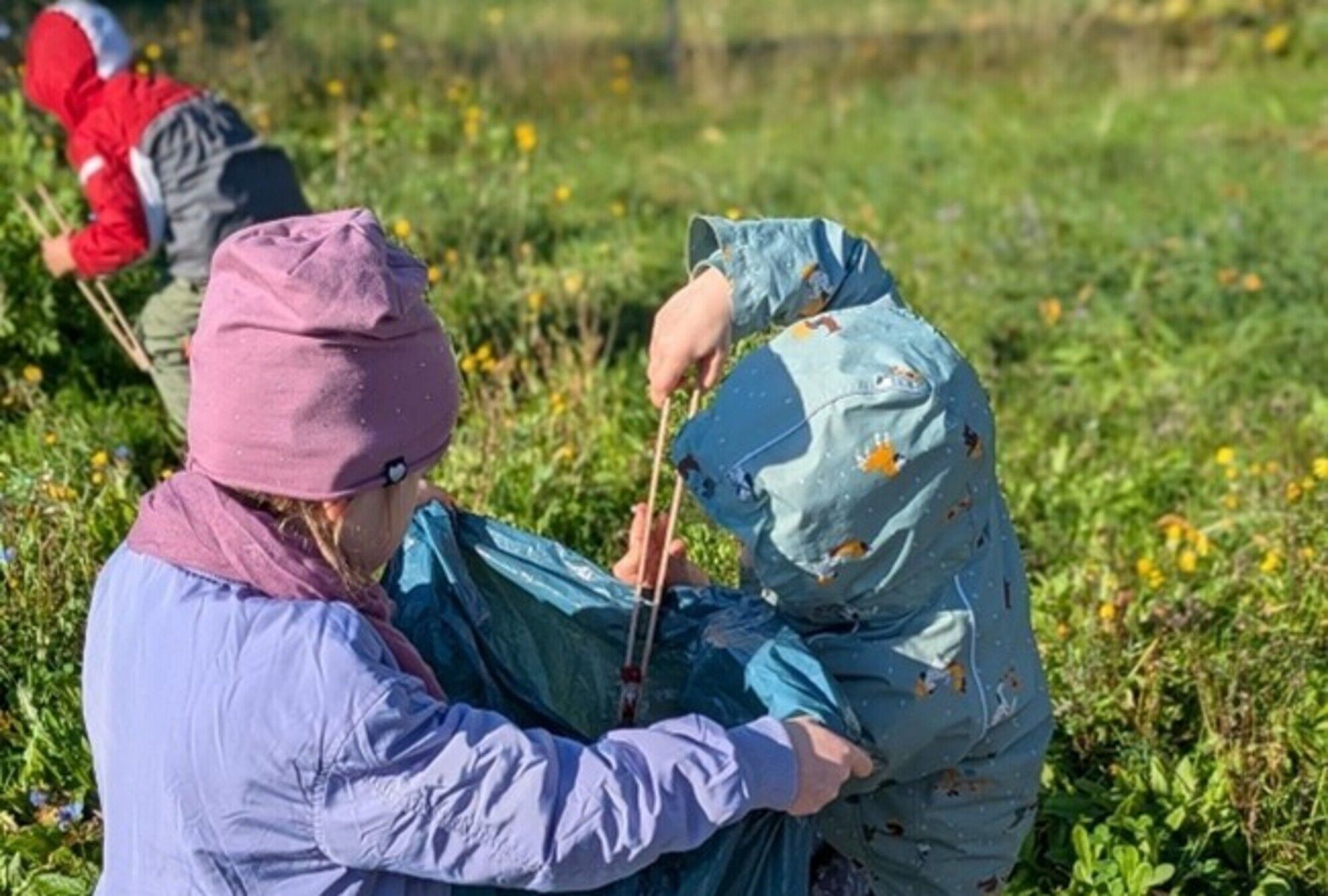Kinder mit Kapuzen packen Müll auf einer Wiese mit einem Müllgreifer in einen Müllsack