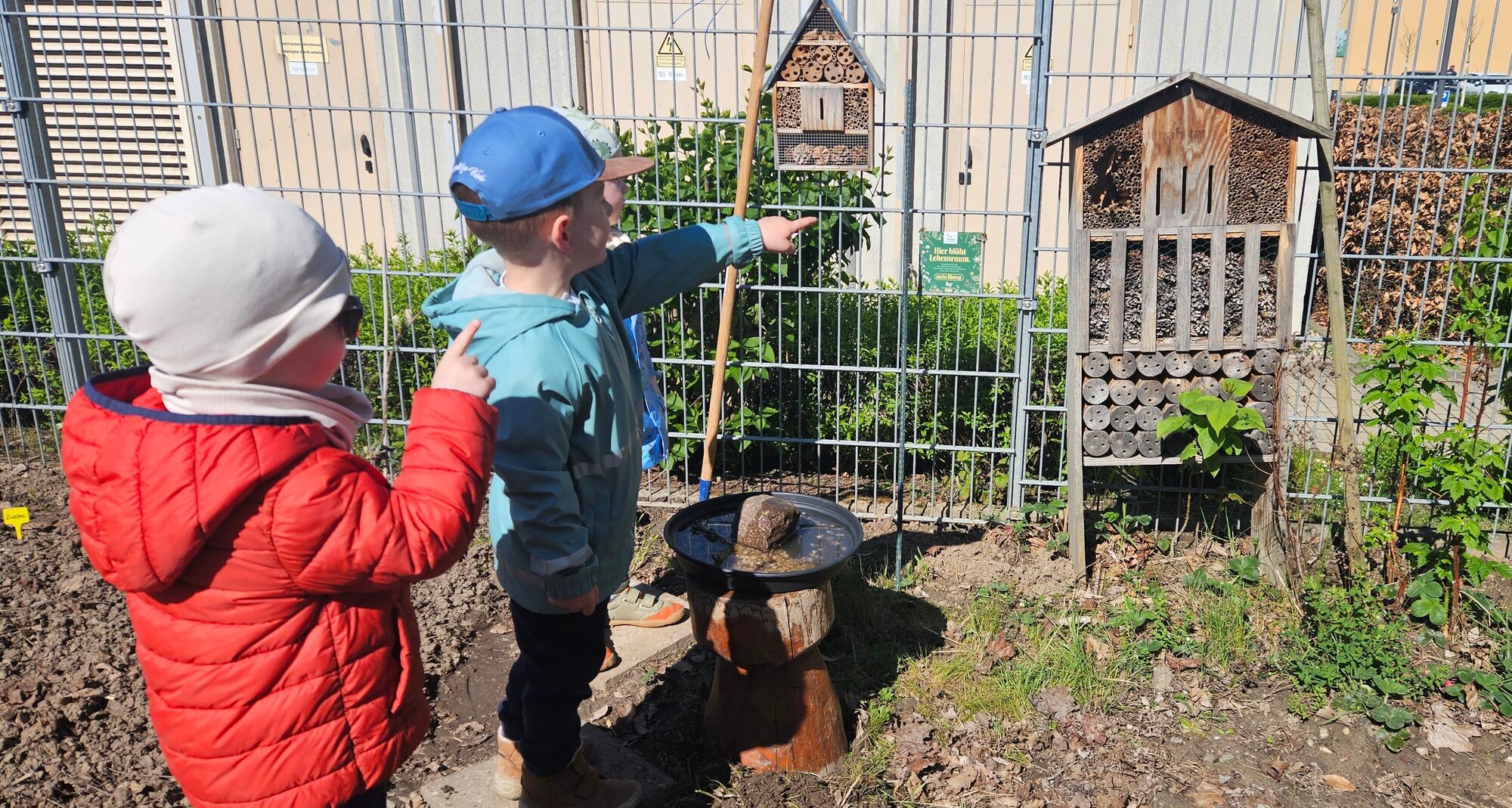 Kinder schauen sich ein Insektenhotel am Zaun an
