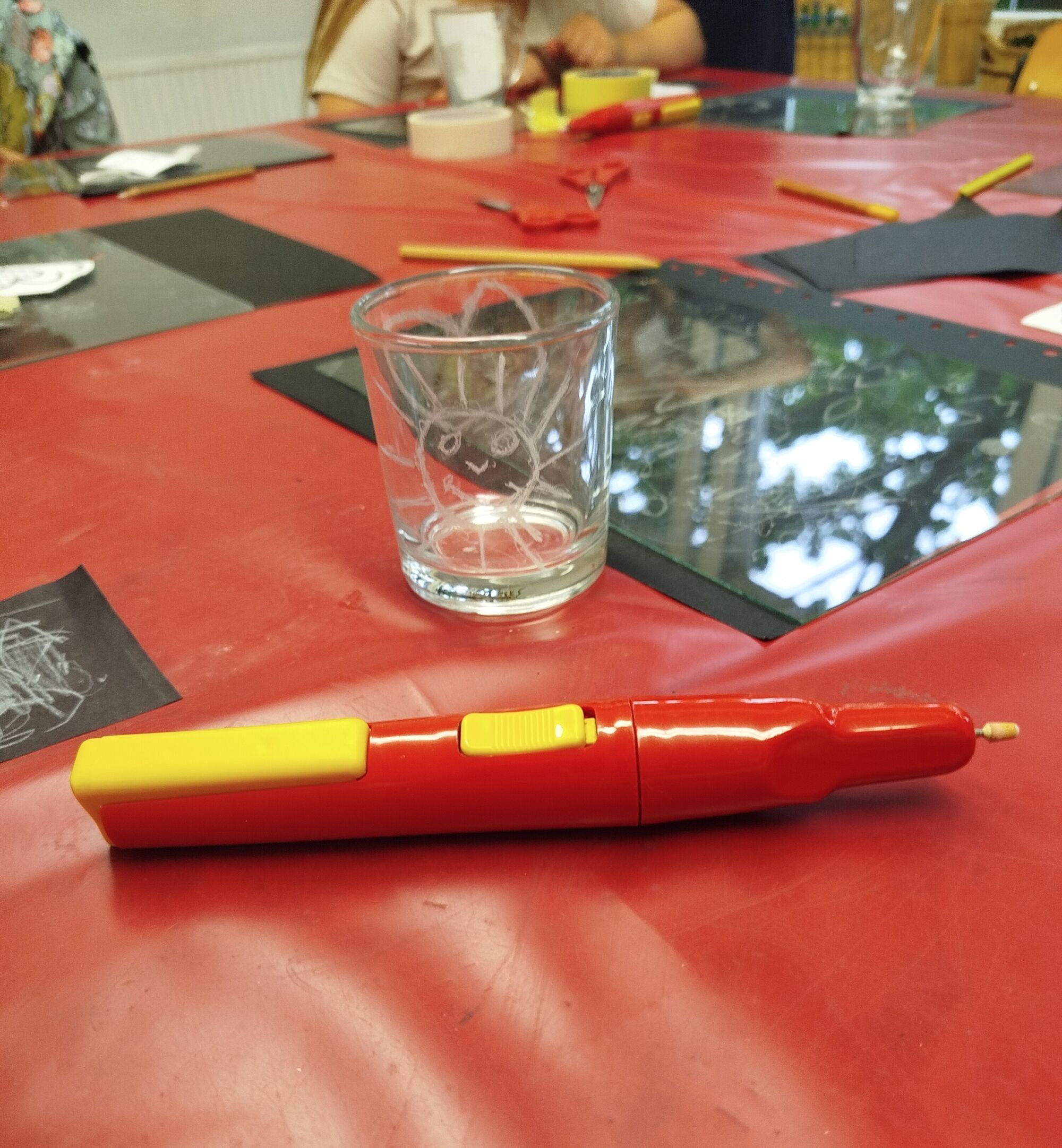 Glänzende Folia, ein elektrischer Stift und ein Glas auf einem roten Wachstischtuch